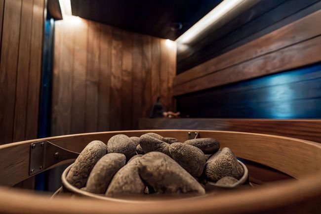 Sauna rivestita in legno con vasca in legno contenente pietre calde in primo piano.