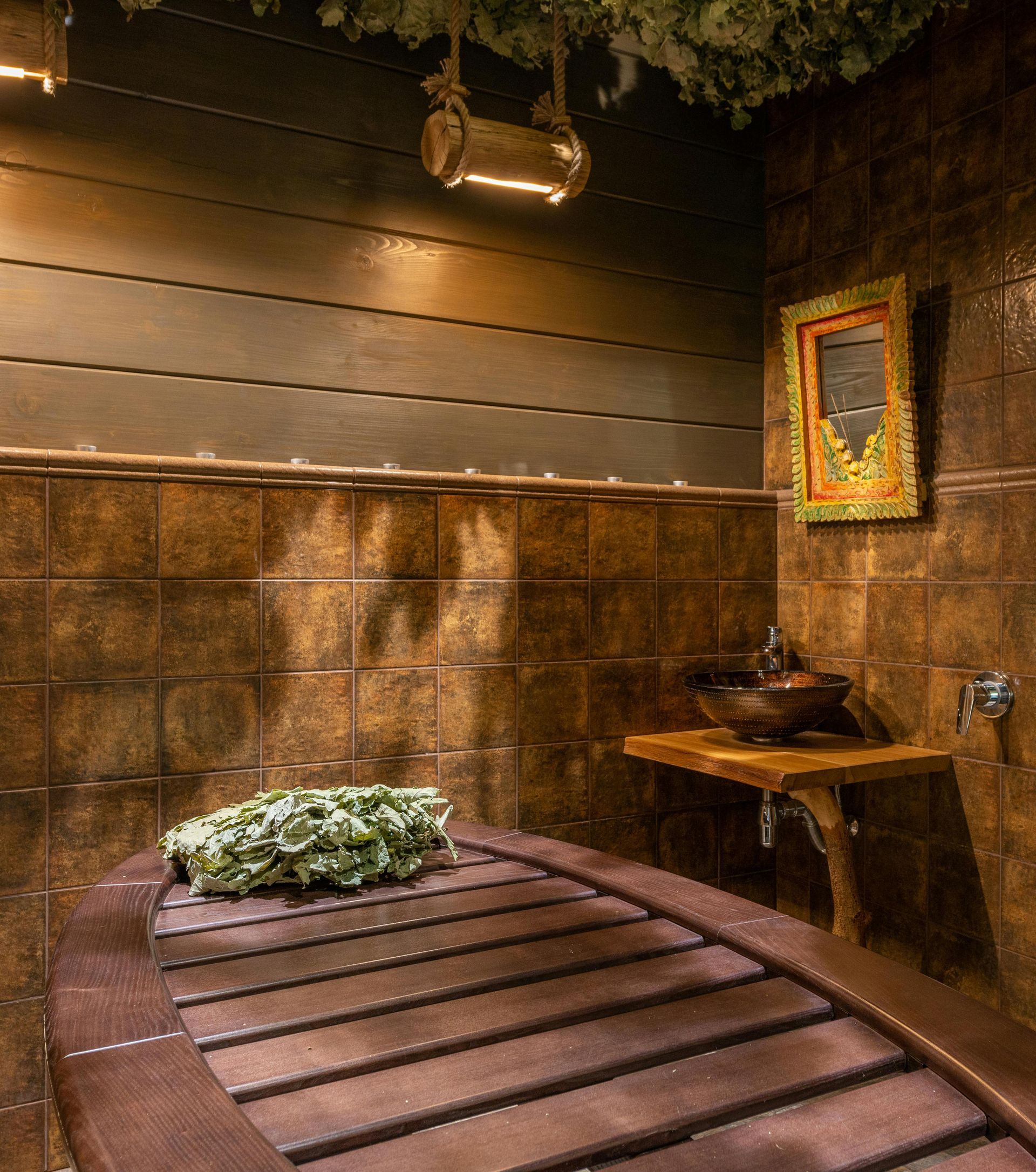 Sauna rivestita in legno con panca in legno, rami frondosi e calda illuminazione ambrata.