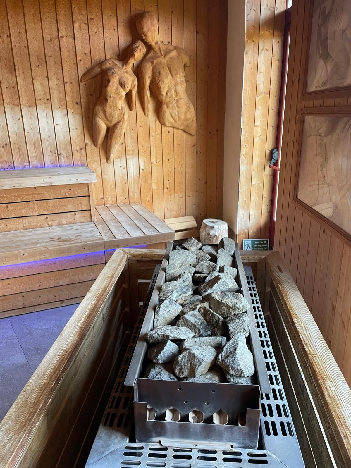 Sauna rivestita in legno con panca e stufa in metallo riempita di pietre per sauna.