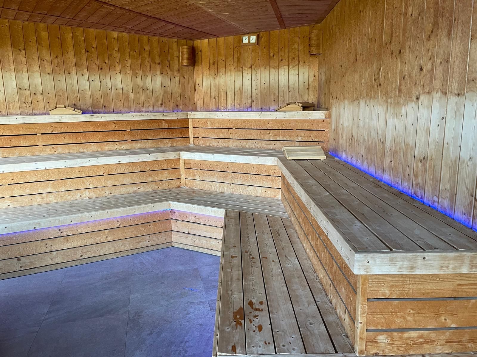 Sauna rivestita in legno con panche a più livelli e illuminazione a LED blu.