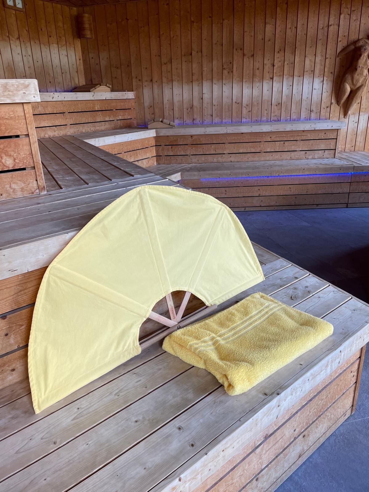 Seggiolino da bagno giallo per neonati e asciugamano su una panca di legno in una stanza simile a una sauna.