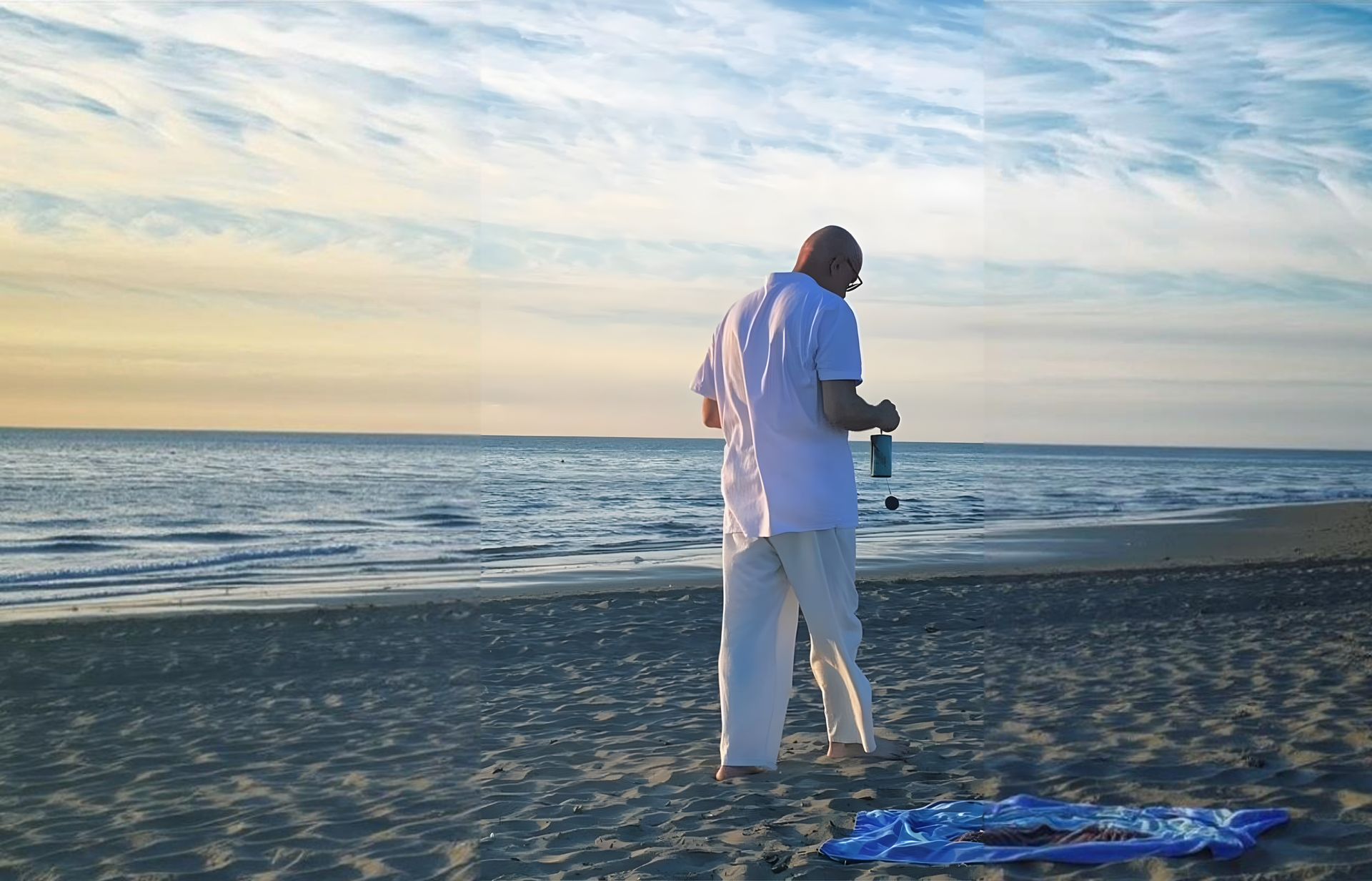 Una persona vestita di bianco si trova su una spiaggia al tramonto e tiene in mano una macchina fotografica.