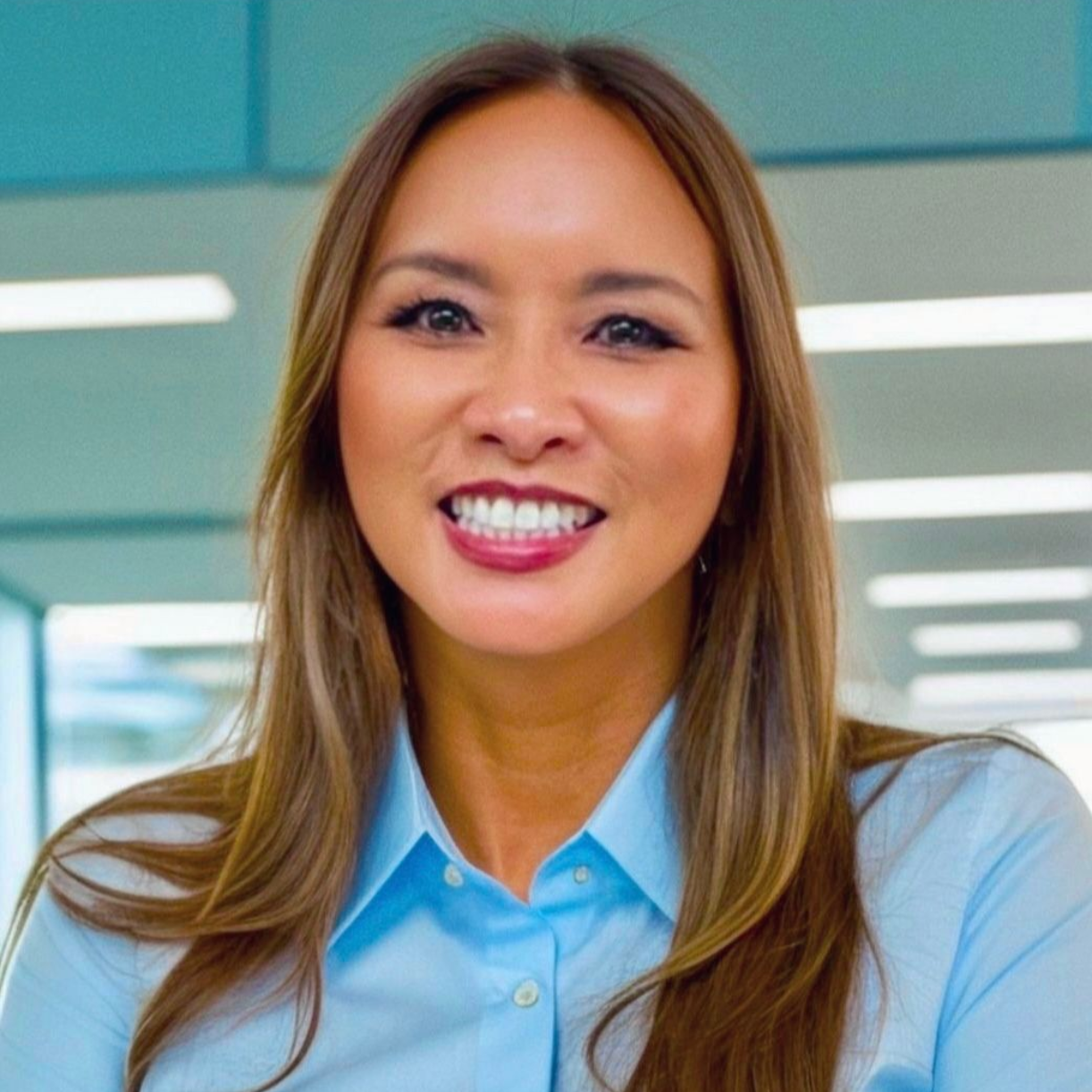 Woman with long brown hair, smiling, wearing a white collared shirt and a gold necklace.