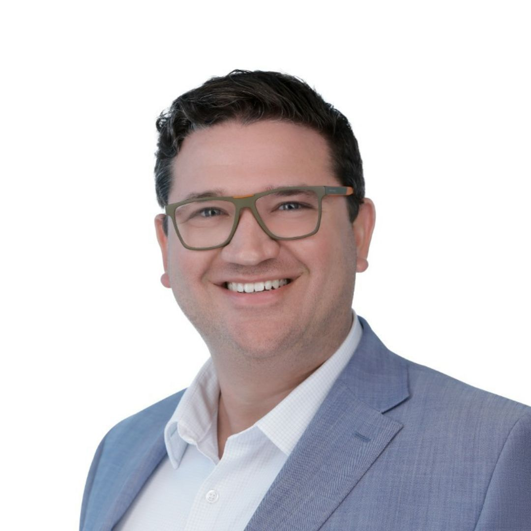 Man with glasses wearing a light blue blazer smiles, against a white background.