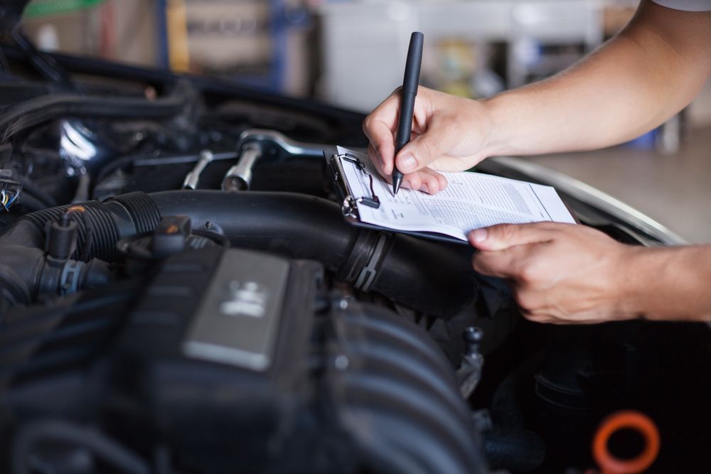 Mechanic Writing on a Notepad Beside a Car Engine During Inspection — Van Diemen's Automotive & Electrical Repairs In Bellerive, TAS