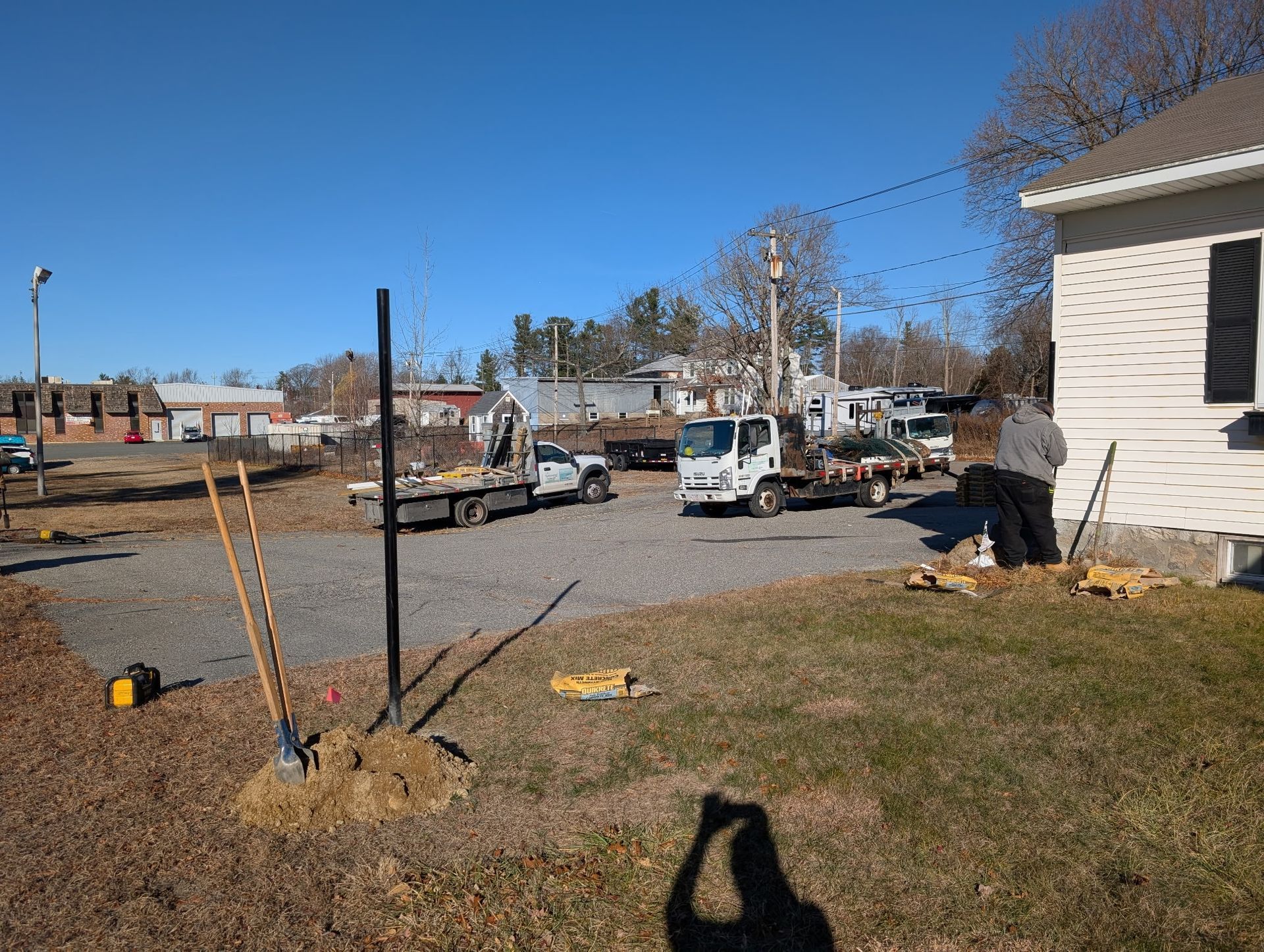 Construction workers near a white building with trucks, gravel, and construction equipment on a sunny day.