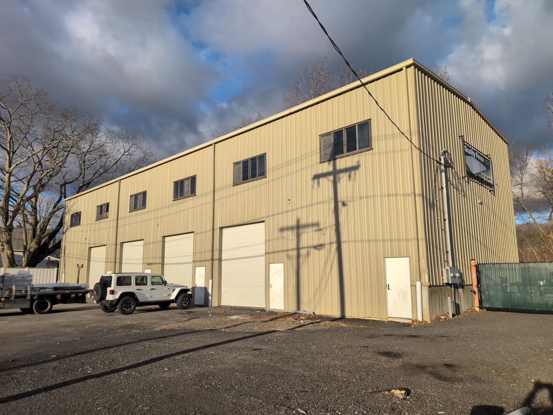 A large, beige industrial warehouse with multiple garage doors and windows, featuring a white SUV parked in front.