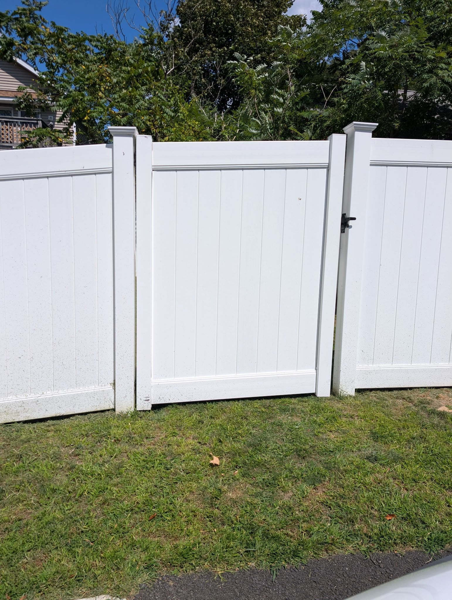 A white vinyl fence with a centered gate, standing over a grassy lawn under a clear blue sky.