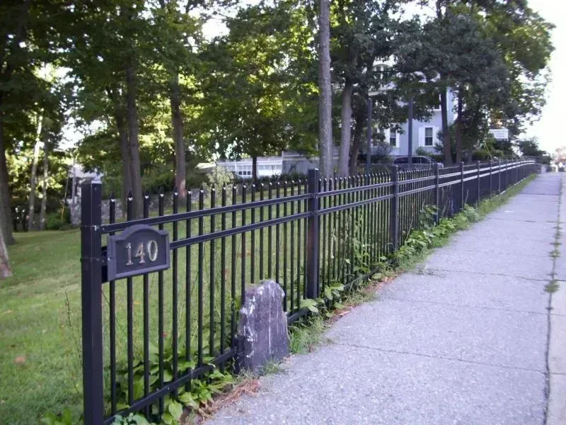A black metal fence runs along a sidewalk, with a sign marked 