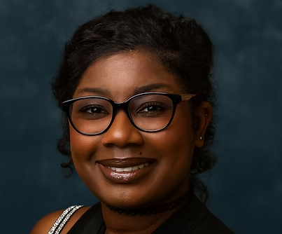 A person with dark hair and glasses smiling against a dark, textured background.