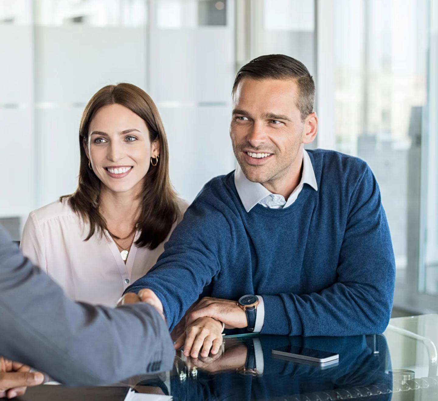 A man and a woman are sitting at a table shaking hands
