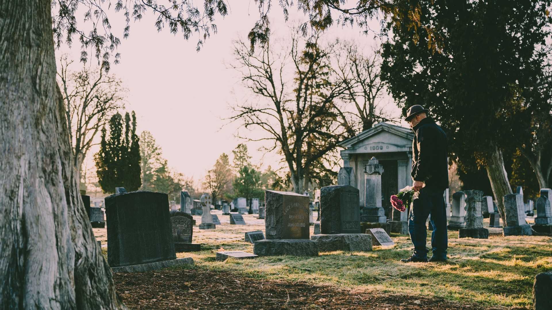 A man is standing in a cemetery holding a bouquet of flowers.