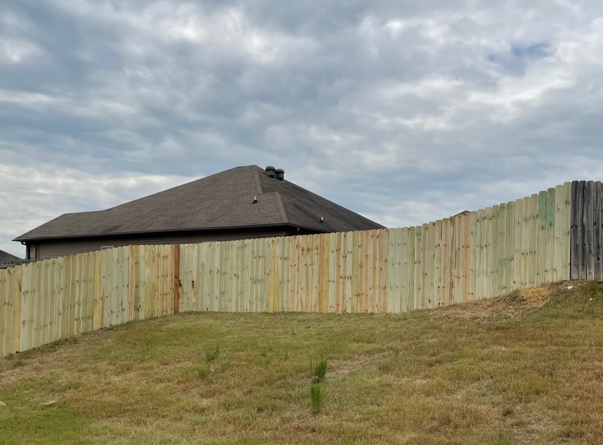 Wooden fence surrounding a house on a grassy hill under a cloudy sky.