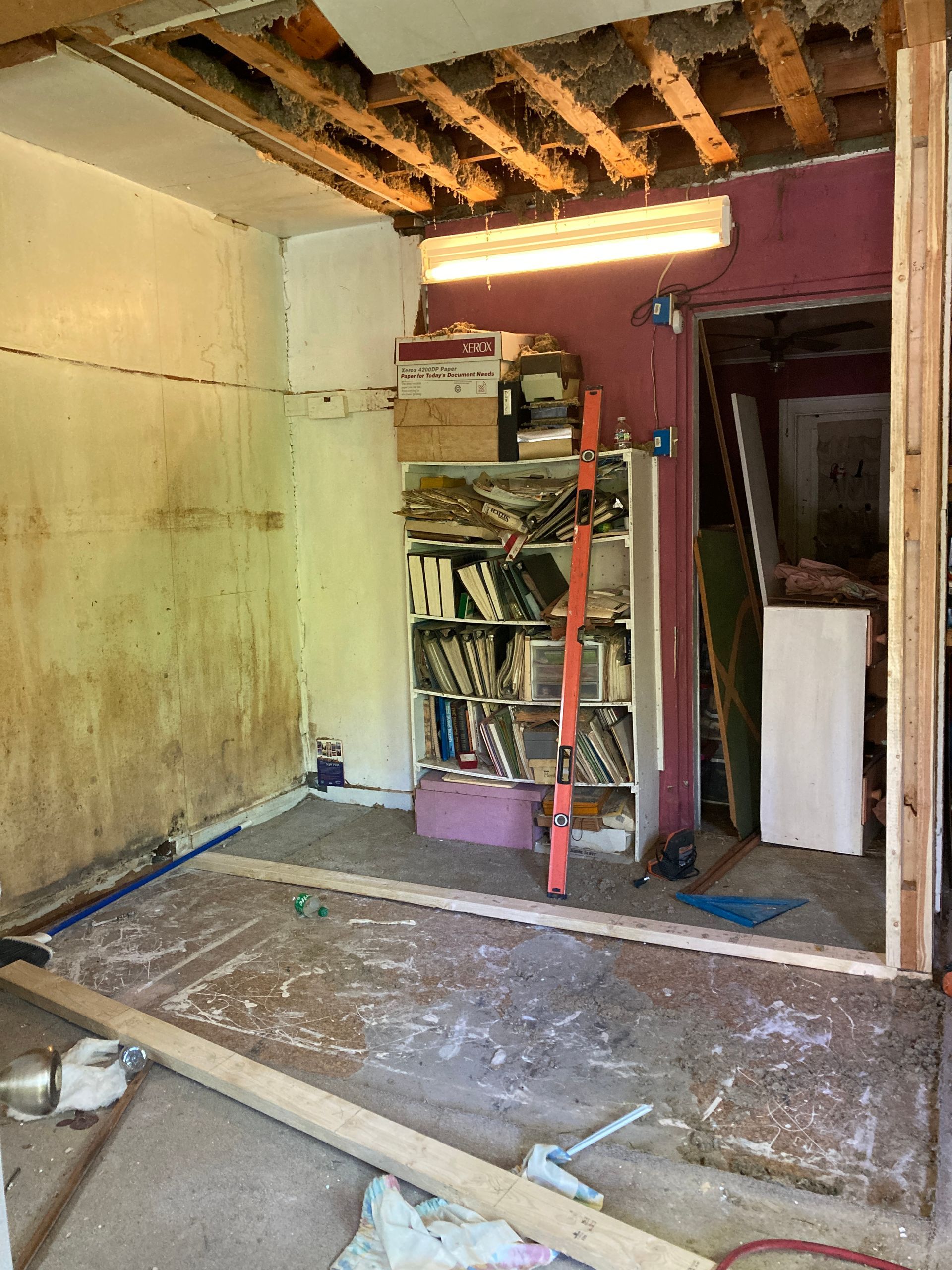 Room under renovation, exposed ceiling beams, bookcase, and tools.