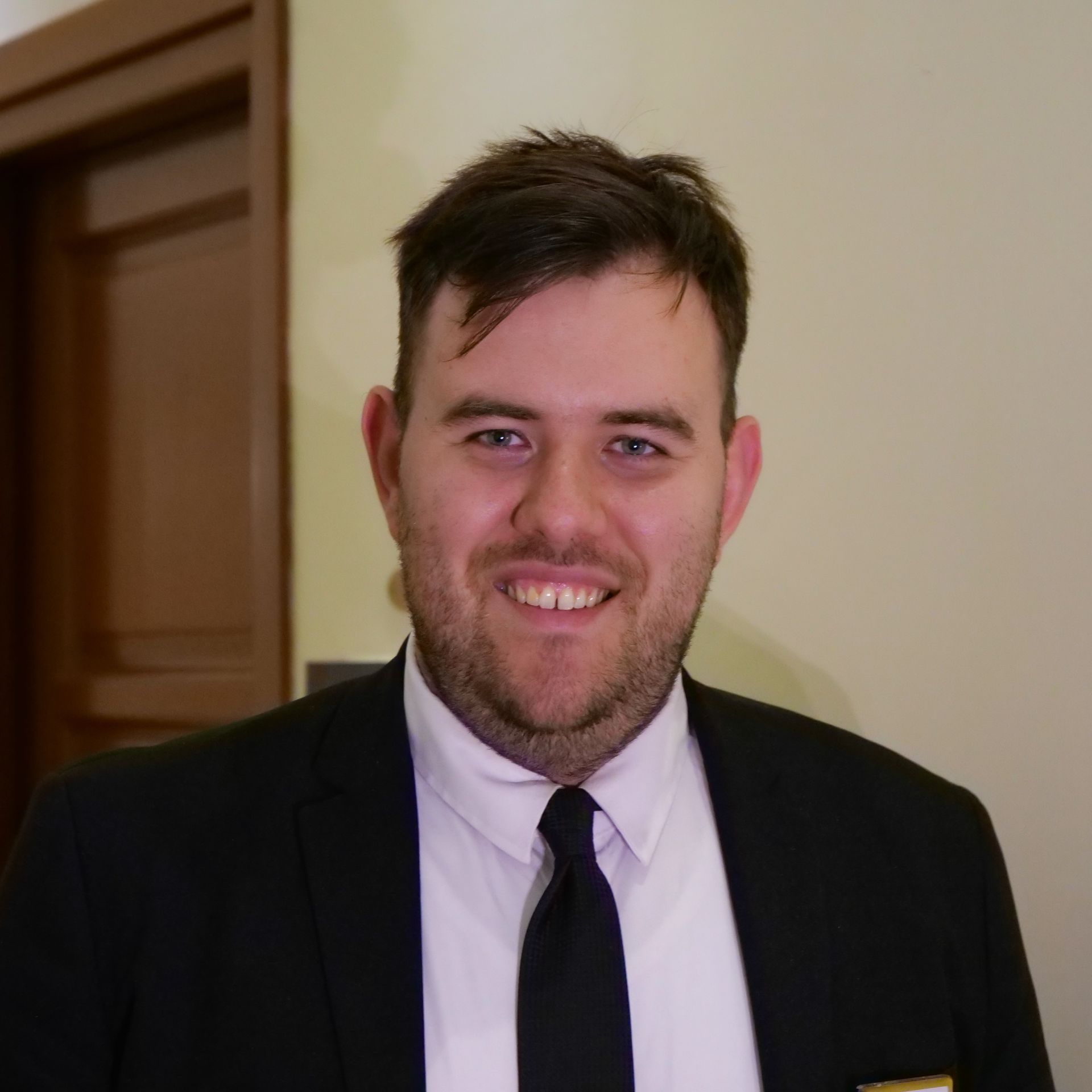 Man wearing a suit and tie, smiling at the camera, inside a building.
