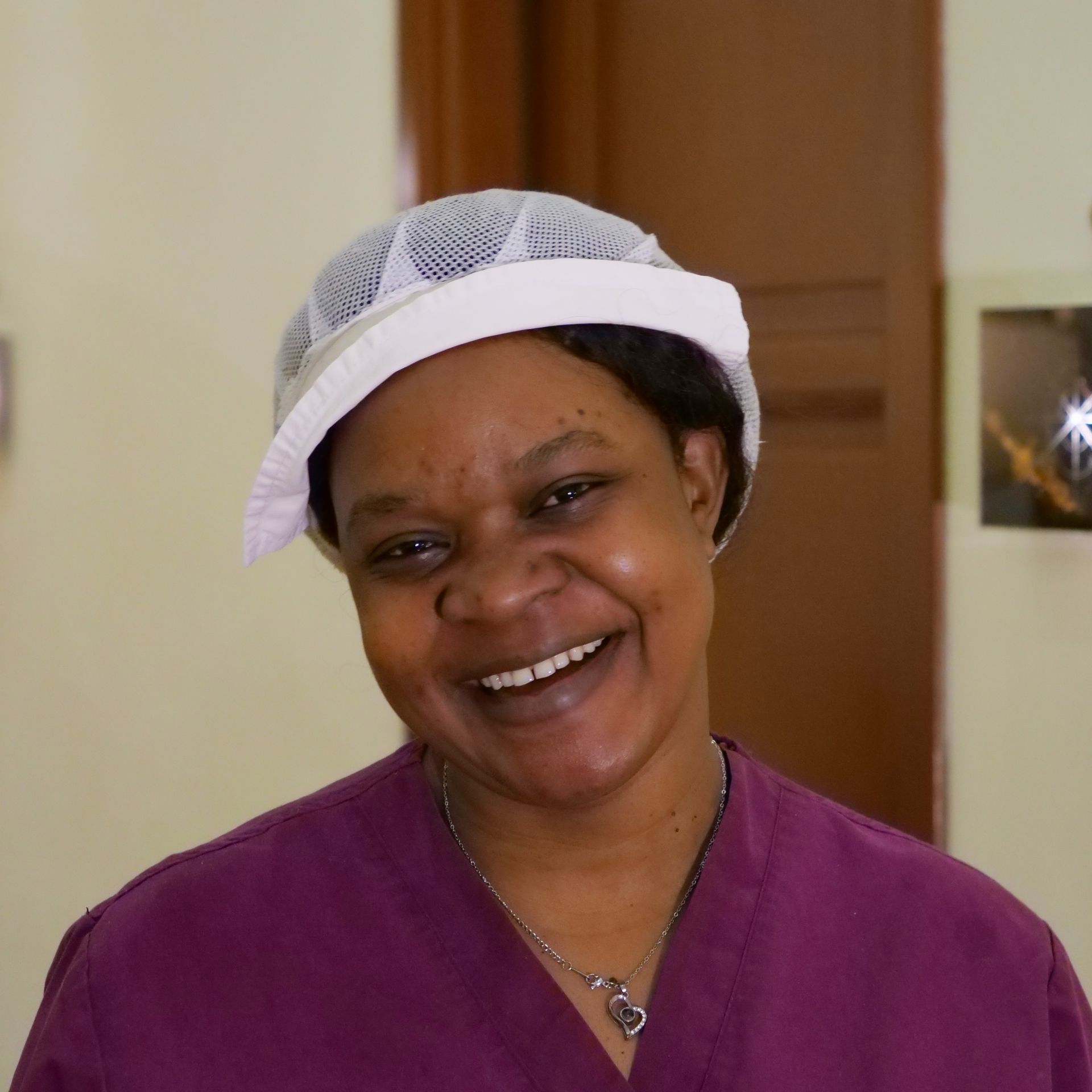 Smiling person in purple scrubs and a white hairnet.