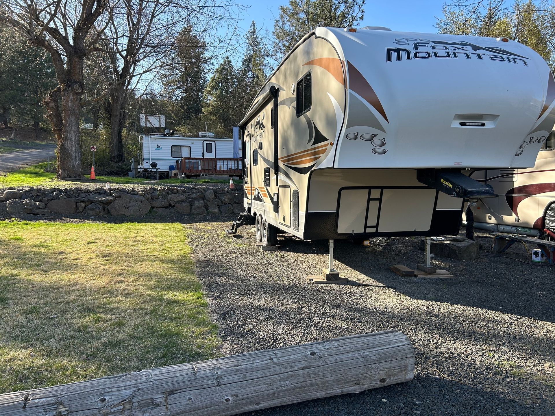 RV parked on gravel, with another trailer in the background. Sunny day.
