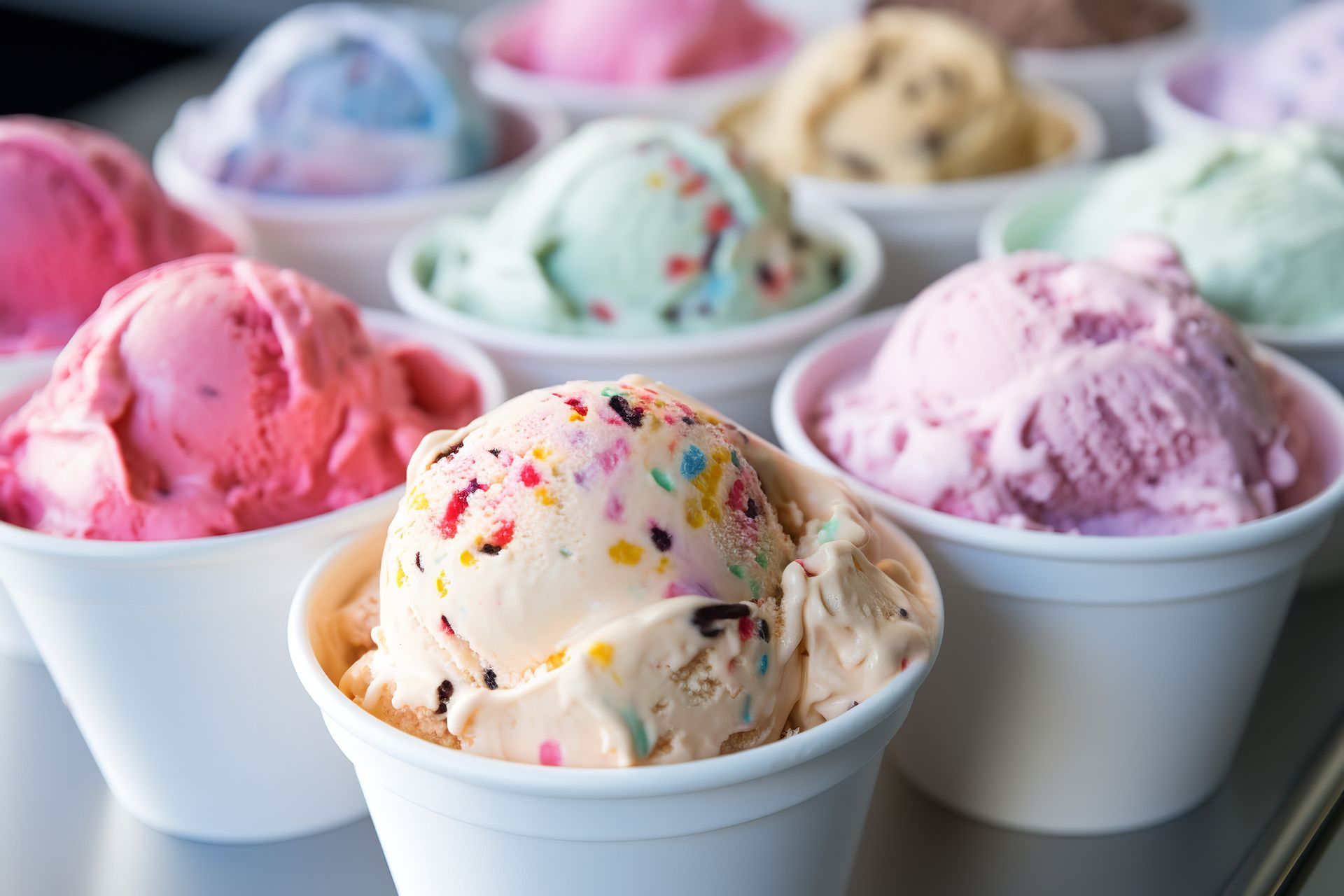 Assorted ice cream scoops in white cups: pink, blue, green, and confetti sprinkled flavors.