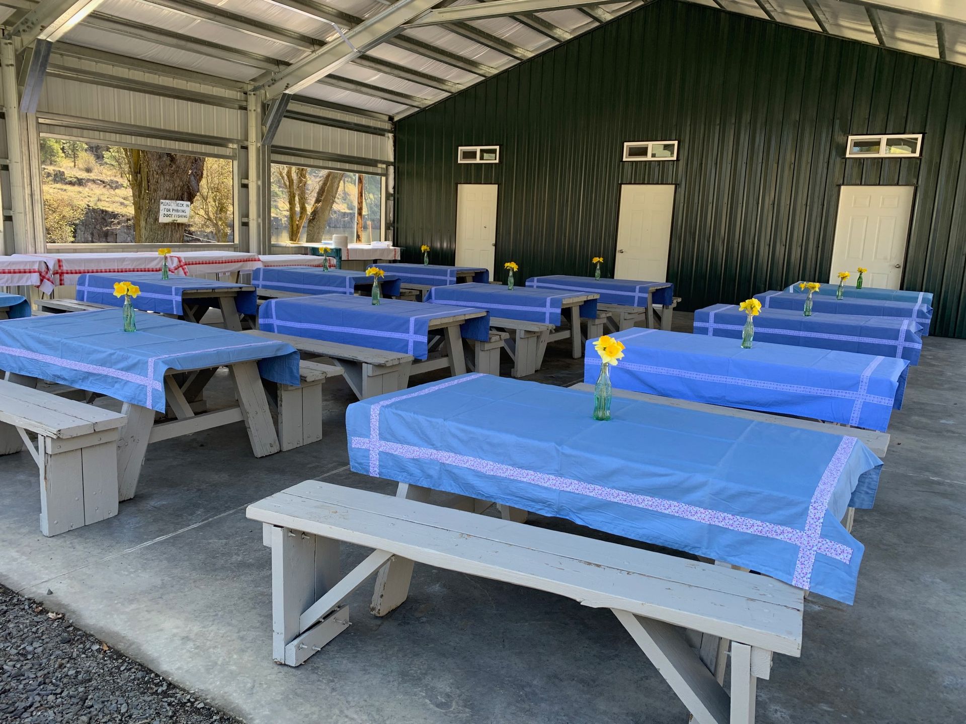 Picnic tables with blue tablecloths set up inside a pavilion, ready for an event.