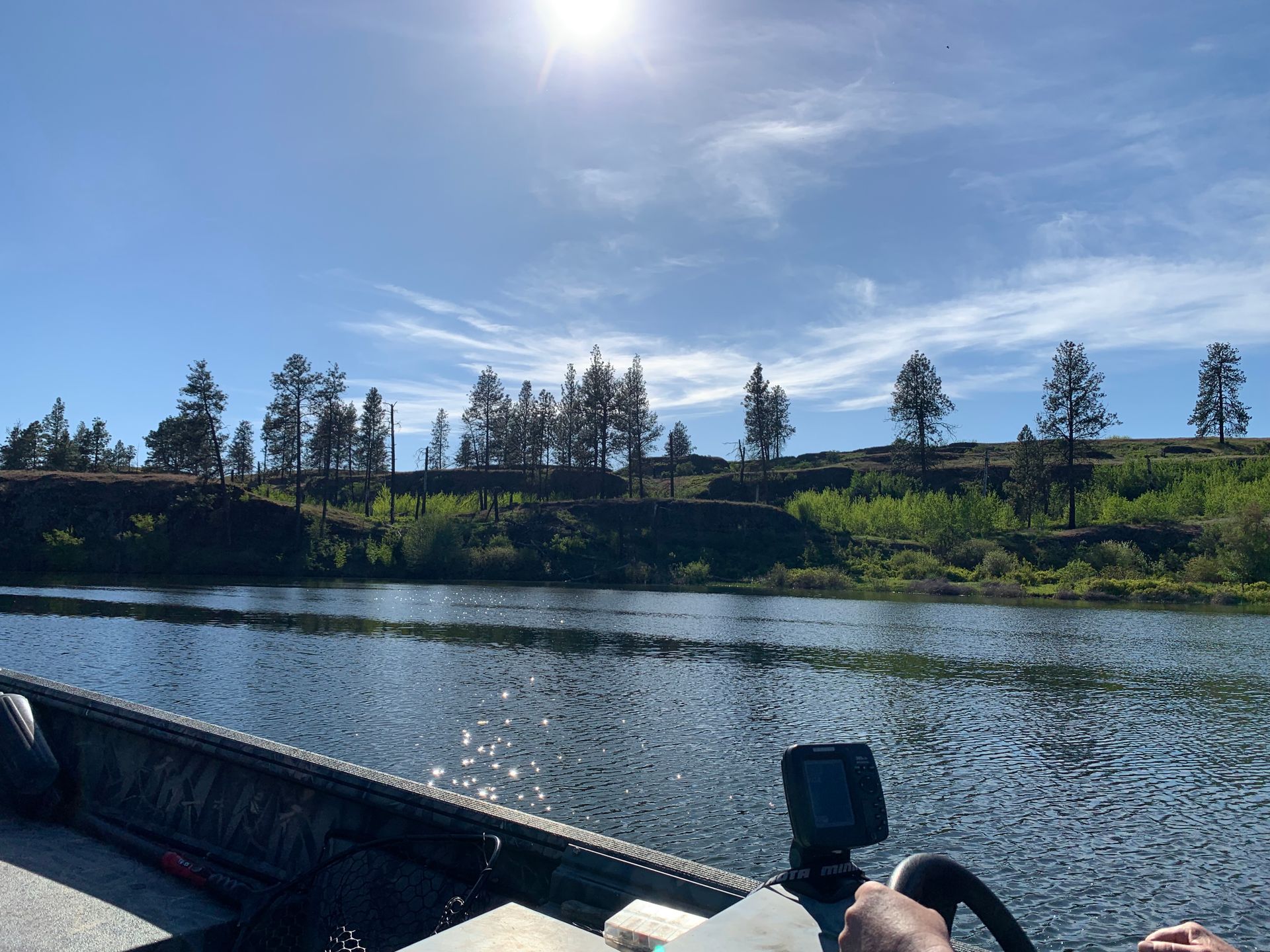 Boat on a river under a bright sun, trees line the distant shore, blue sky.