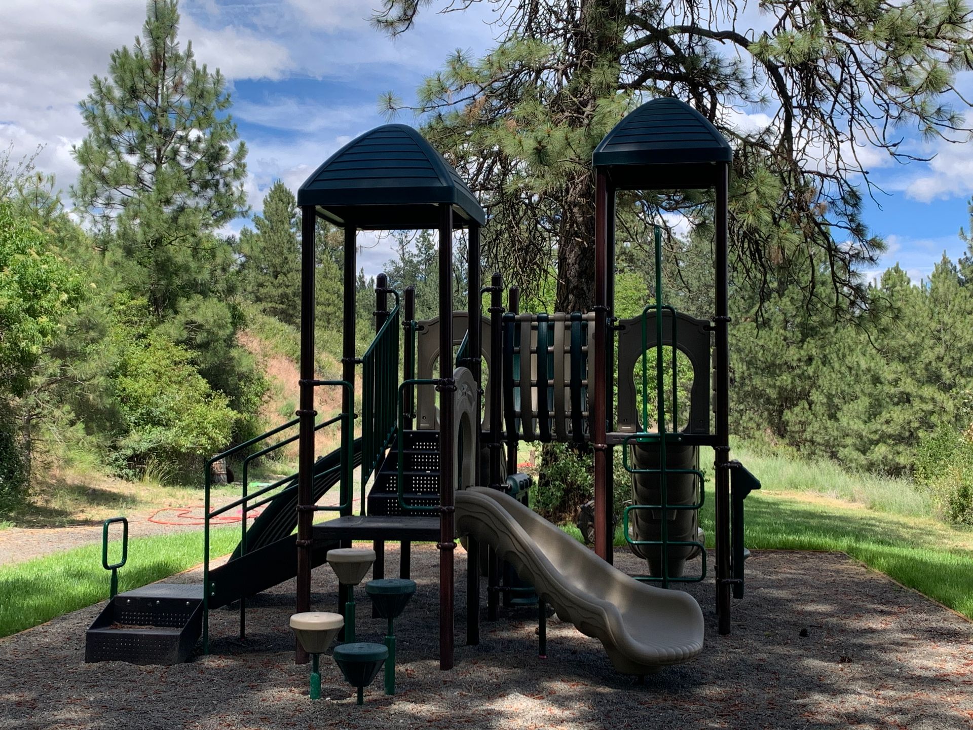 Playground structure with slides, steps, and towers in a park setting.