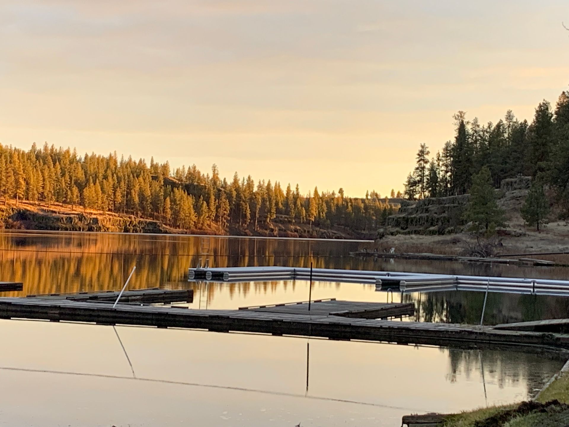 Calm lake with dock at sunset; golden light reflects on the water and trees on the shore.