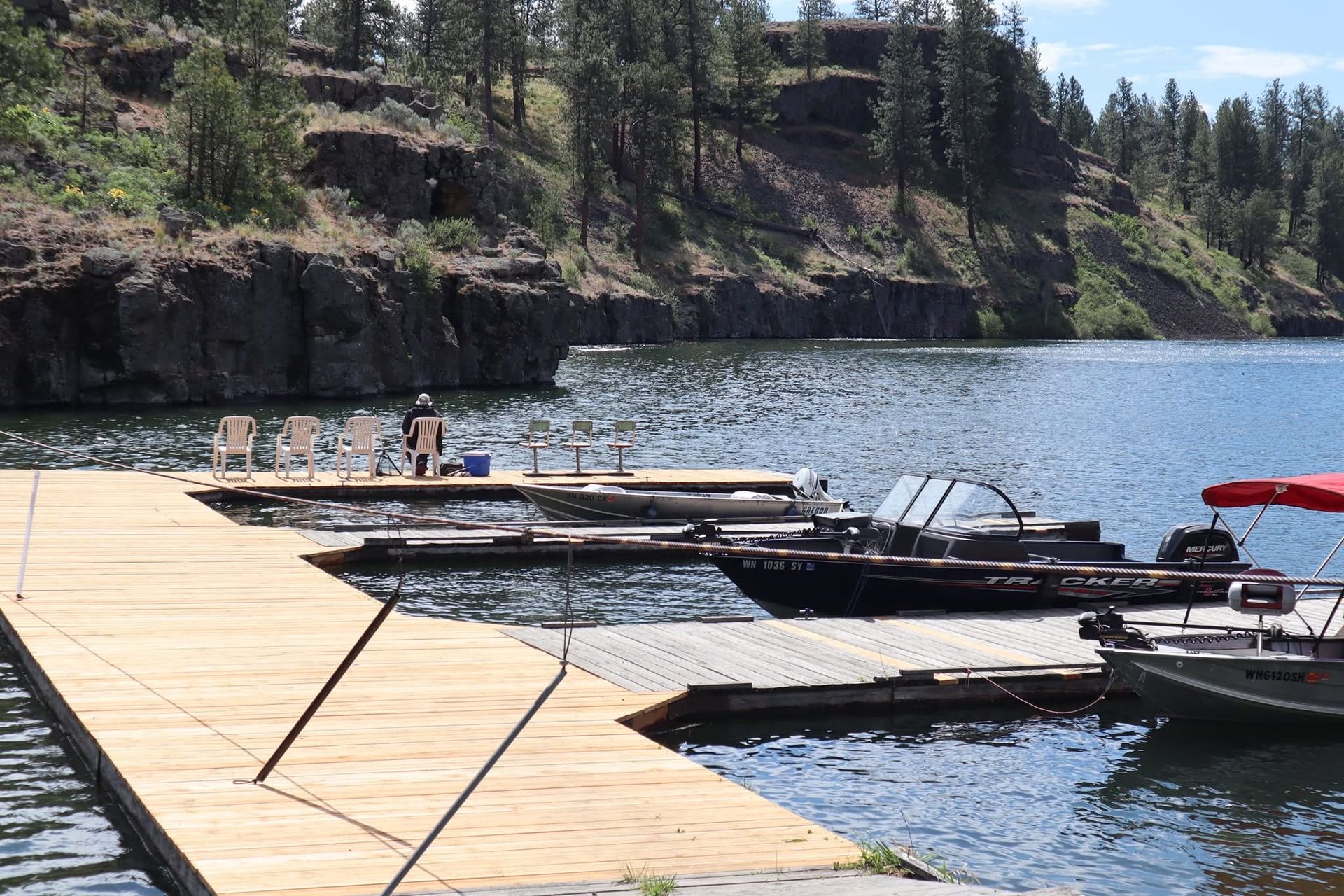 Wooden dock with boats on a lake; rocky cliff backdrop.