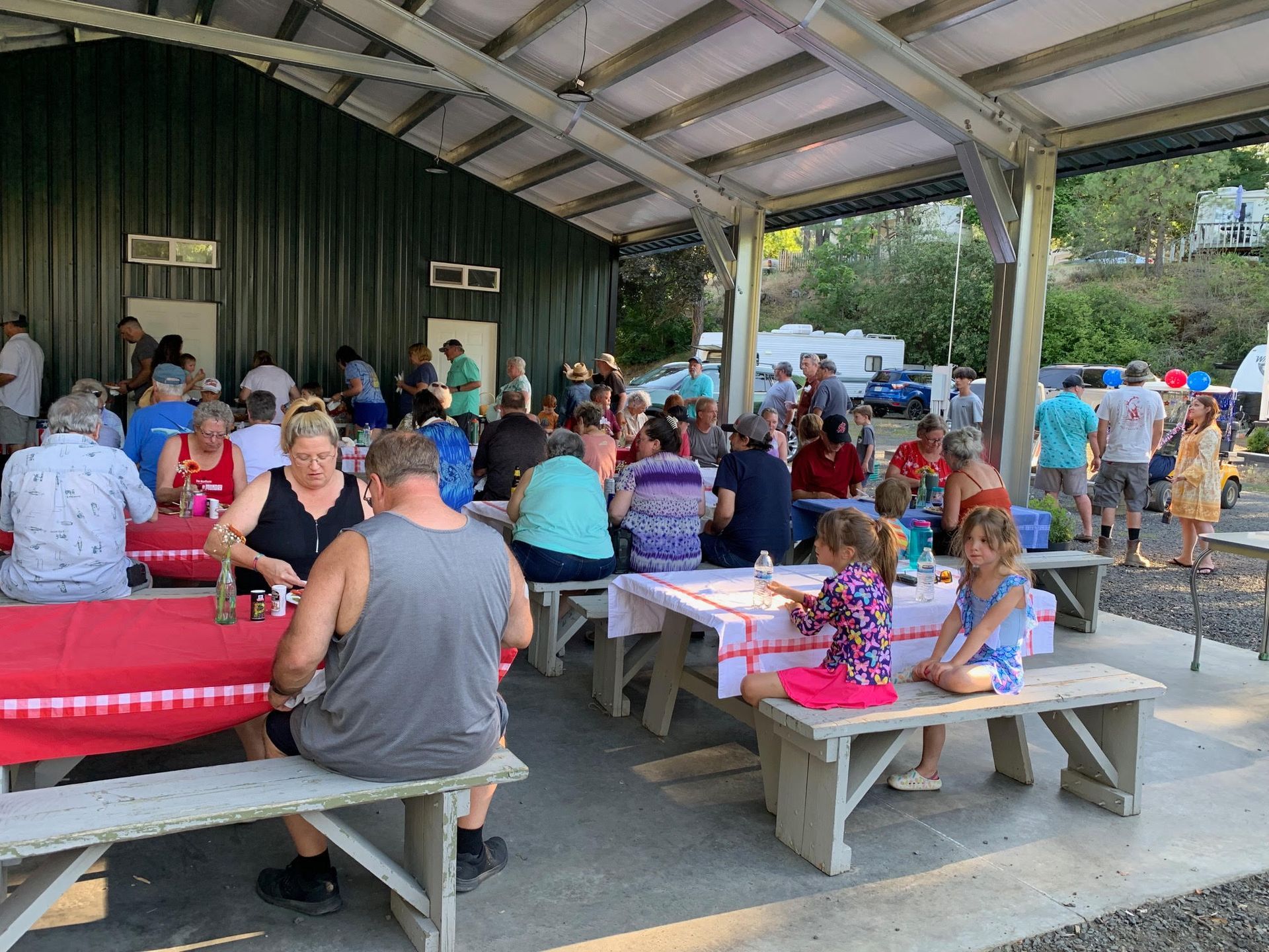 People at picnic tables under a covered shelter, enjoying an outdoor gathering.