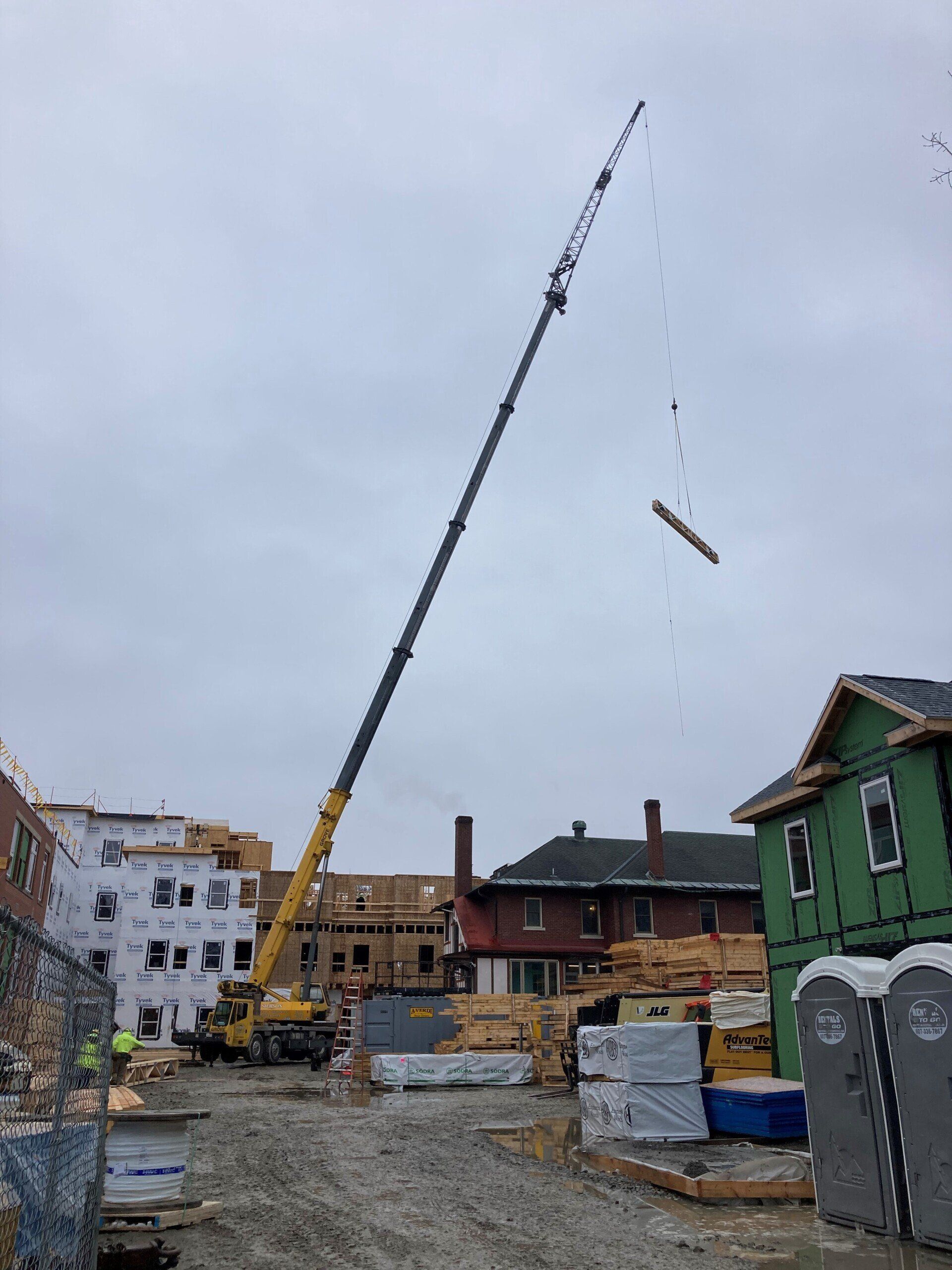 Construction crane lifting lumber at a building site with cloudy sky in the background.