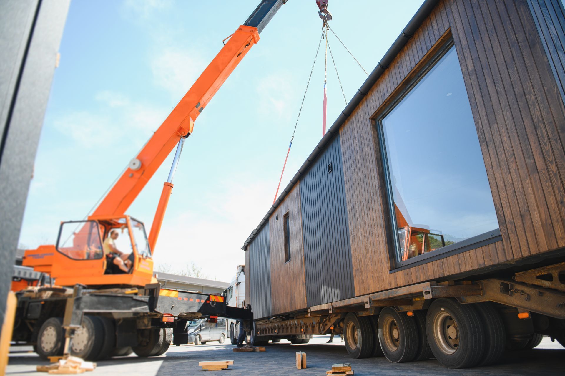 Crane lifting prefabricated modular house onto truck for transportation.