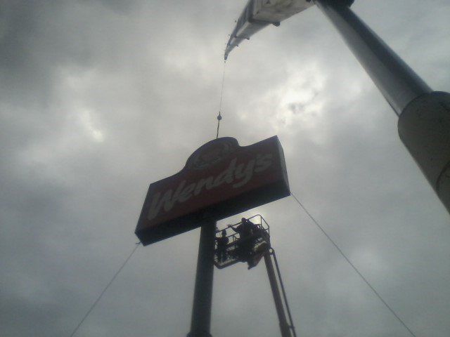 A Wendy's sign being worked on by a person in a lift against a cloudy sky.