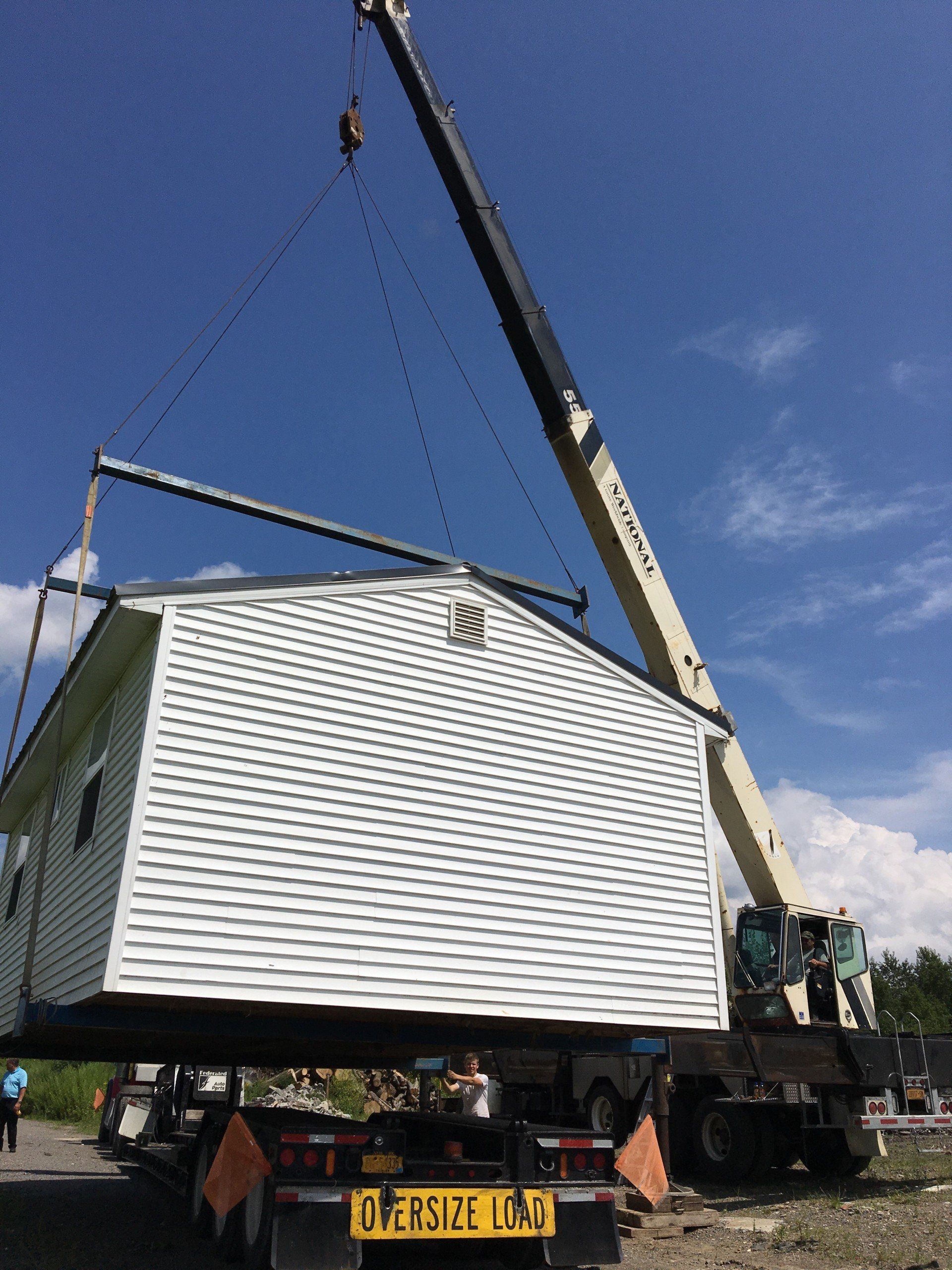 A crane lifting a white modular home onto a truck with an 