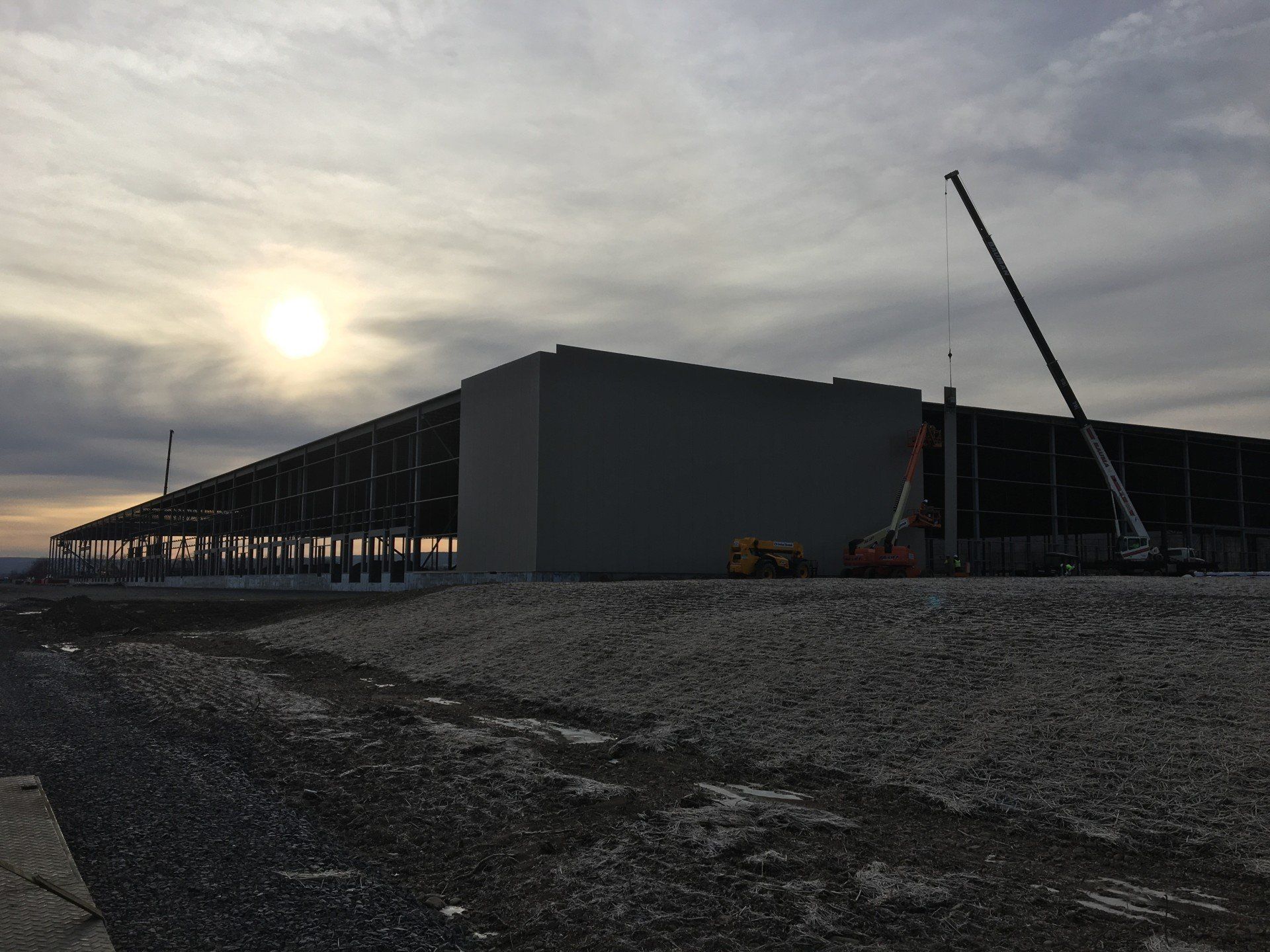 Construction site with a large building under development at dusk, a crane is present.