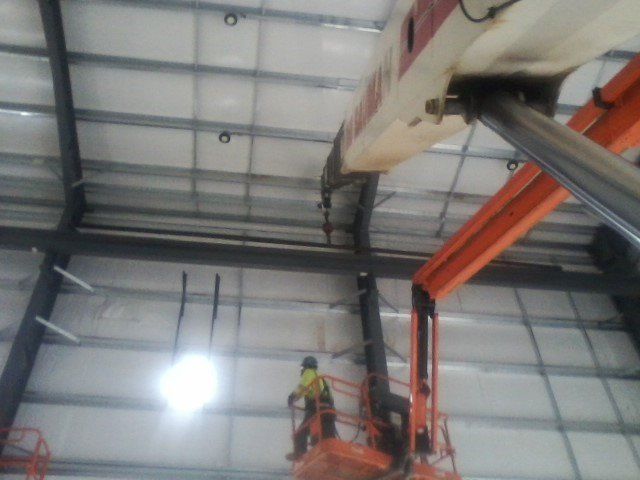 Worker in lift near airplane wing in hangar. Orange lift, white building with black beams.