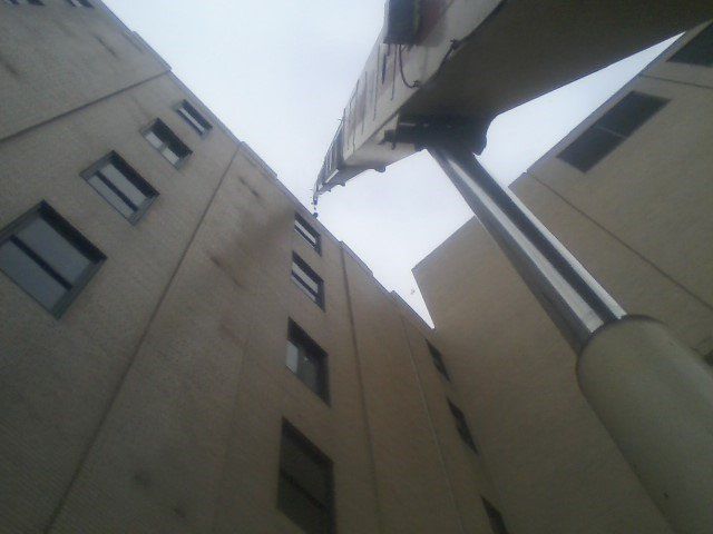 Low-angle view of beige buildings with windows, a large, cylindrical pole, and cloudy sky.