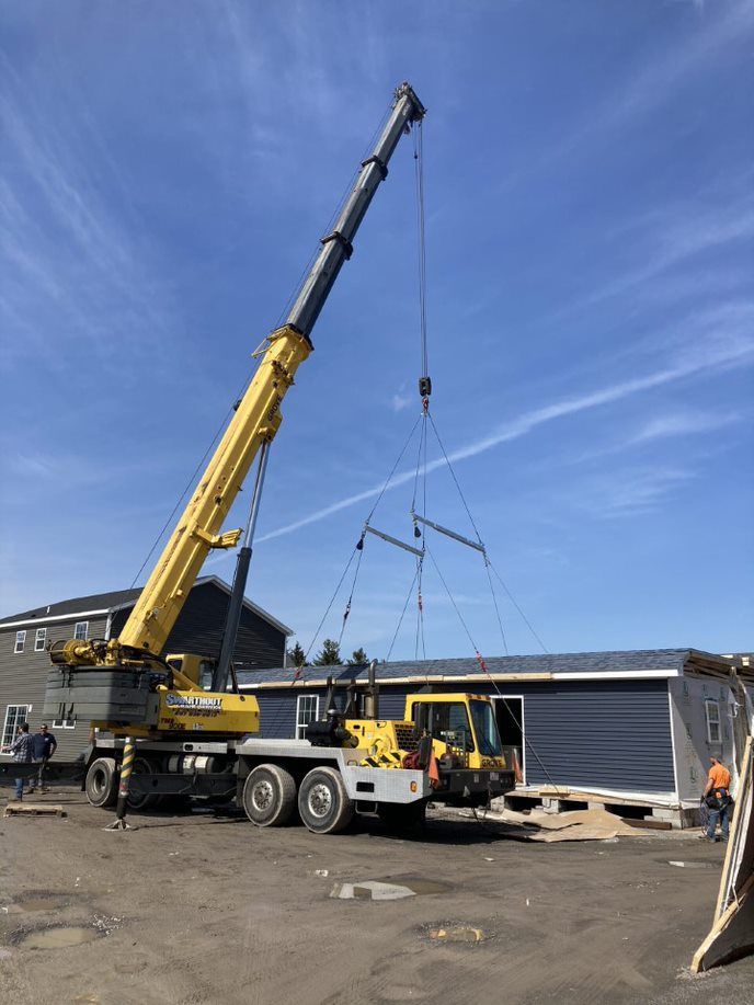 Yellow crane lifting a dark blue modular building on a sunny day. Construction site.