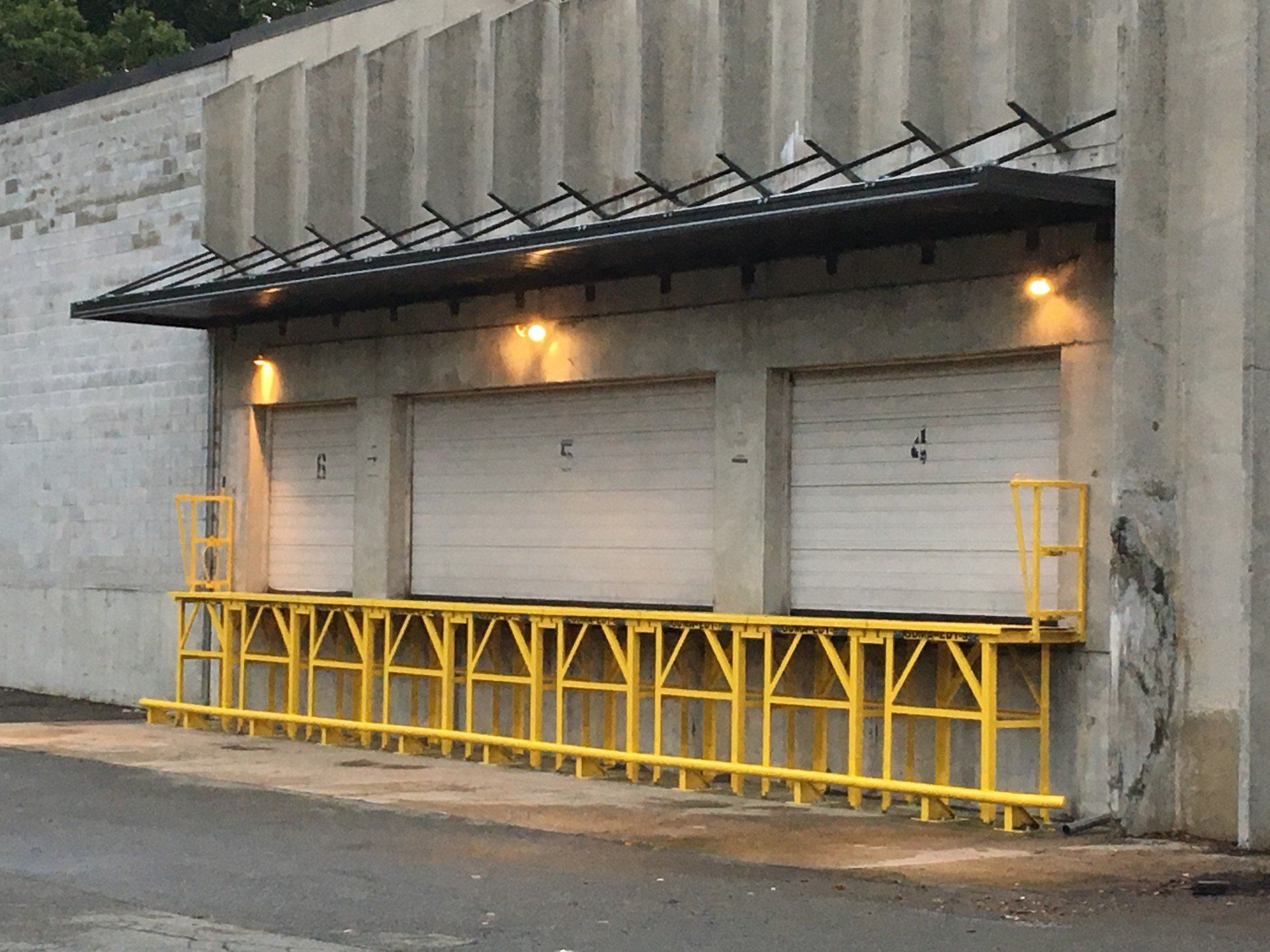 Loading docks with three closed white doors, a yellow platform, and a black awning.