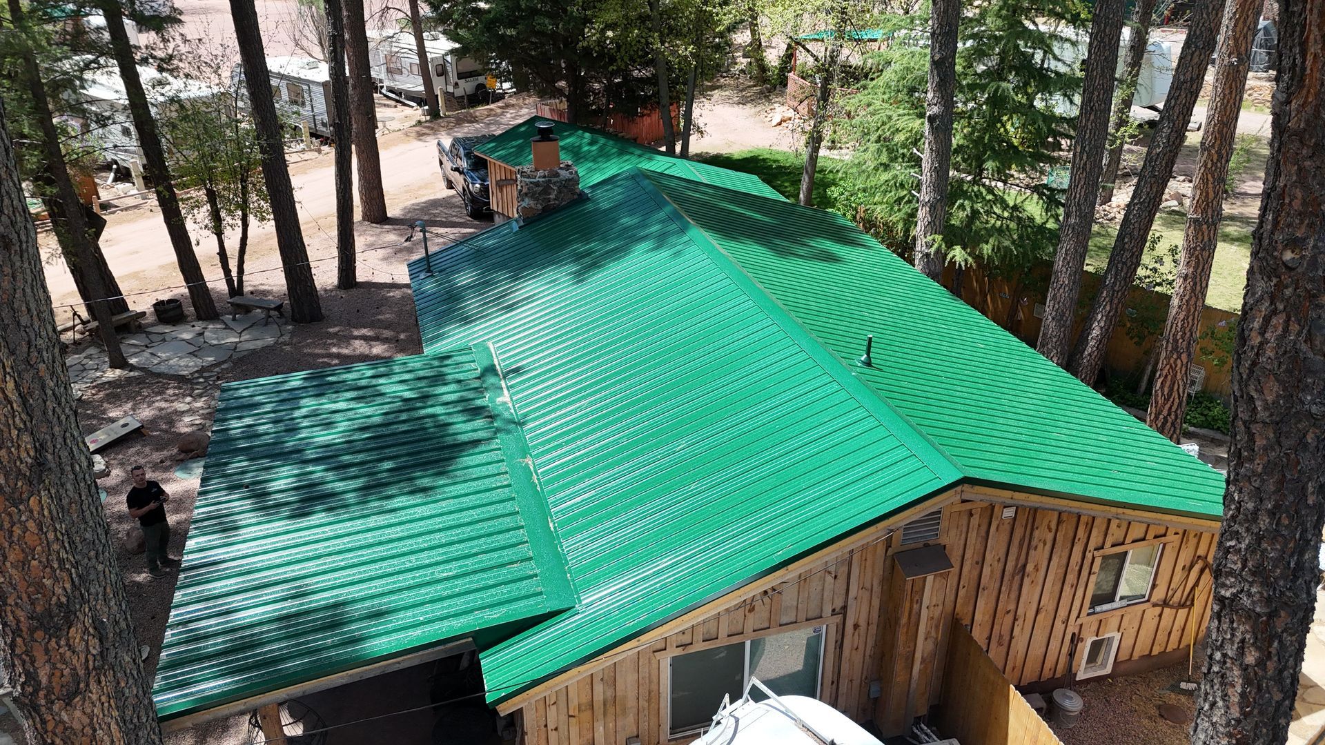 An aerial view of a house with a green roof surrounded by trees.
