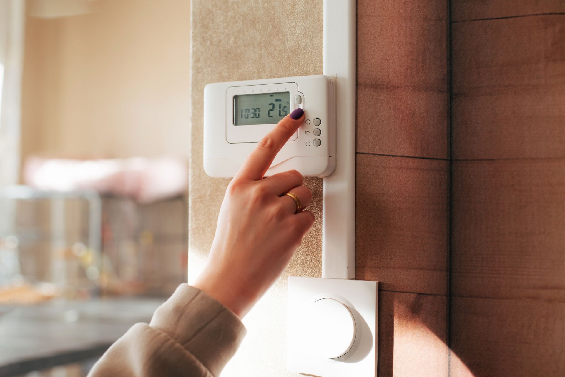 A woman is adjusting the temperature on a thermostat.