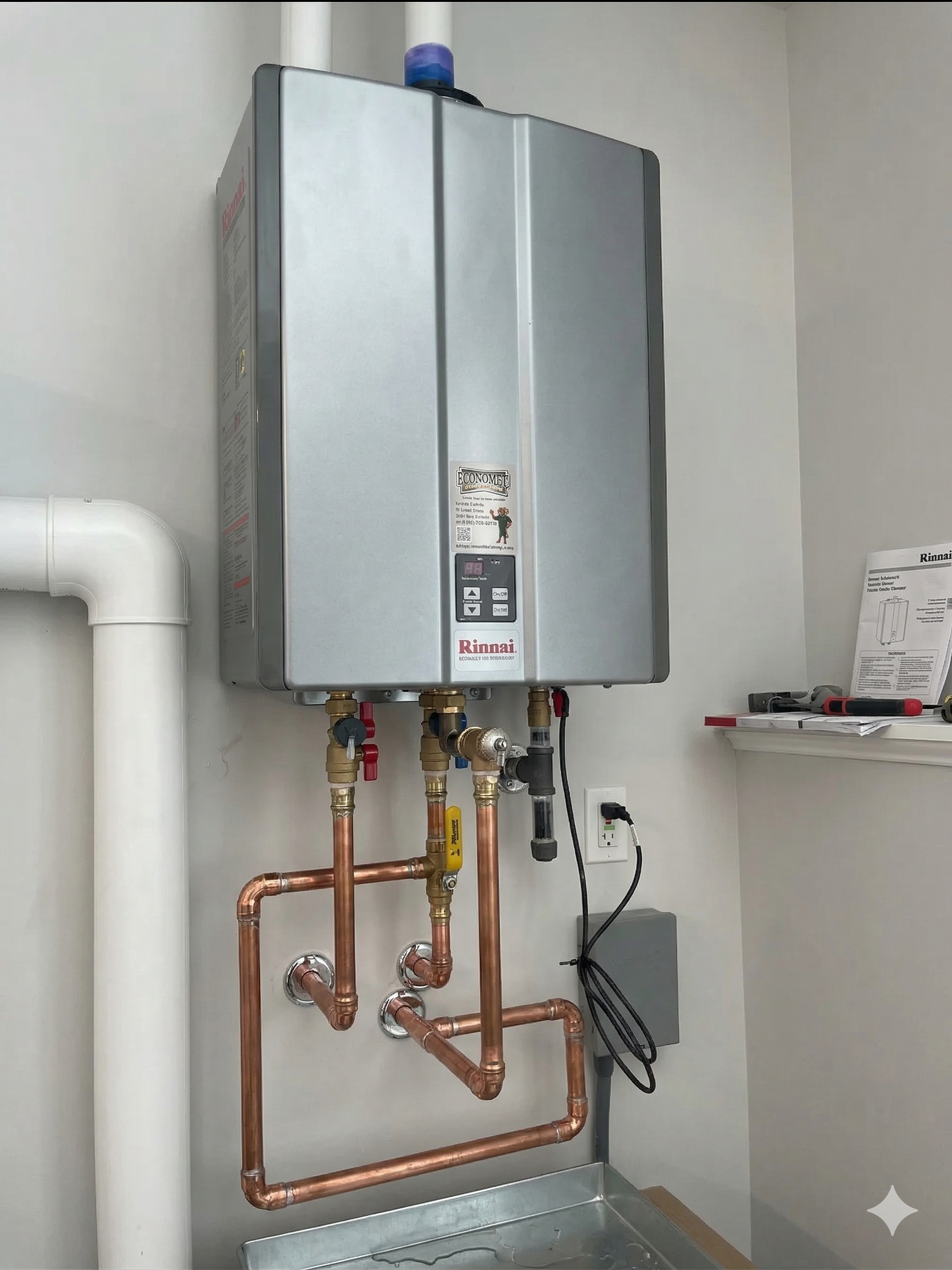 A Navien tankless water heater mounted on a gray wall with copper plumbing pipes, isolation valves, and white vent pipes.
