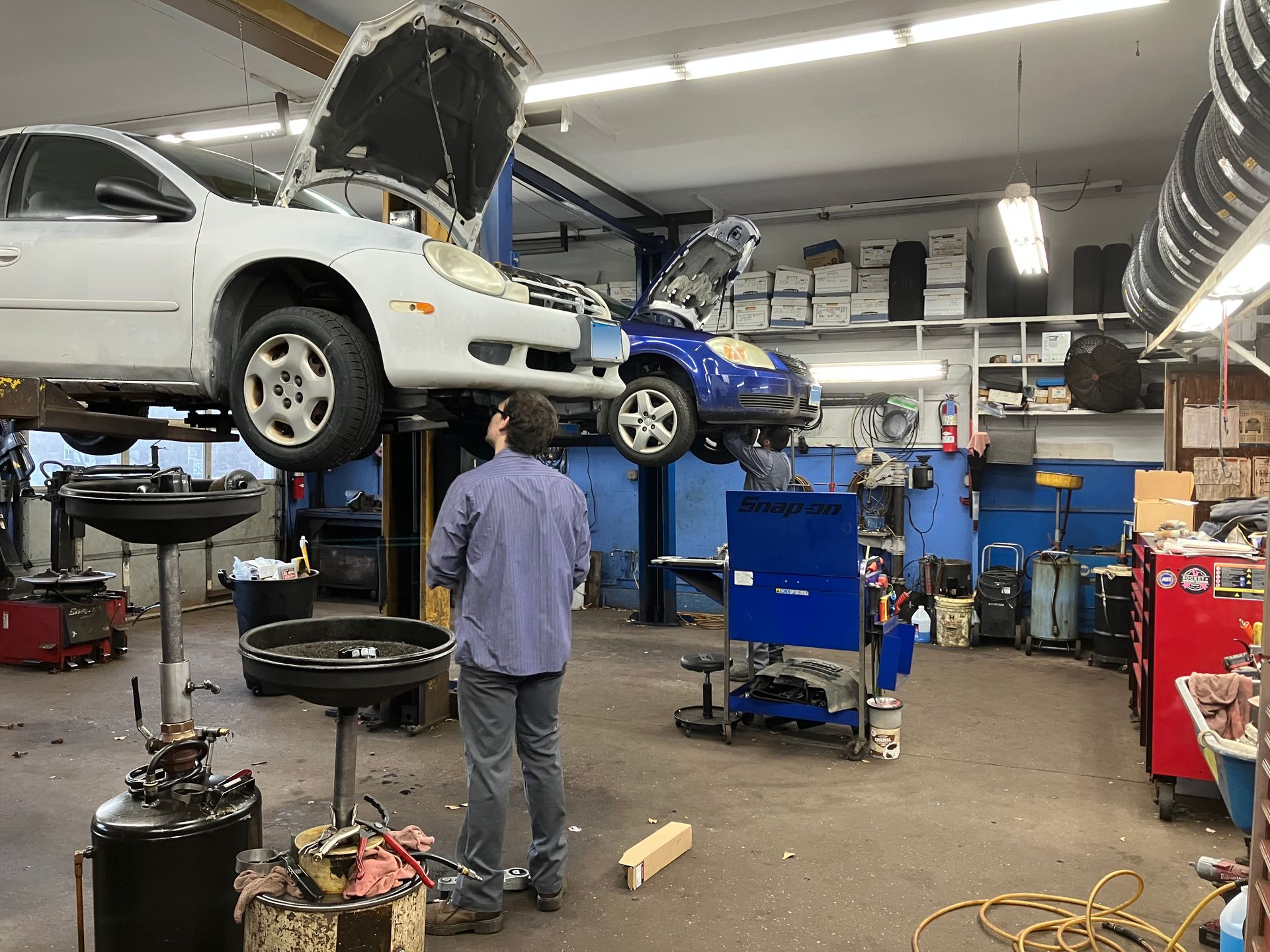 Mechanic in a garage, working on cars lifted on hoists.  | Broadway Auto Service