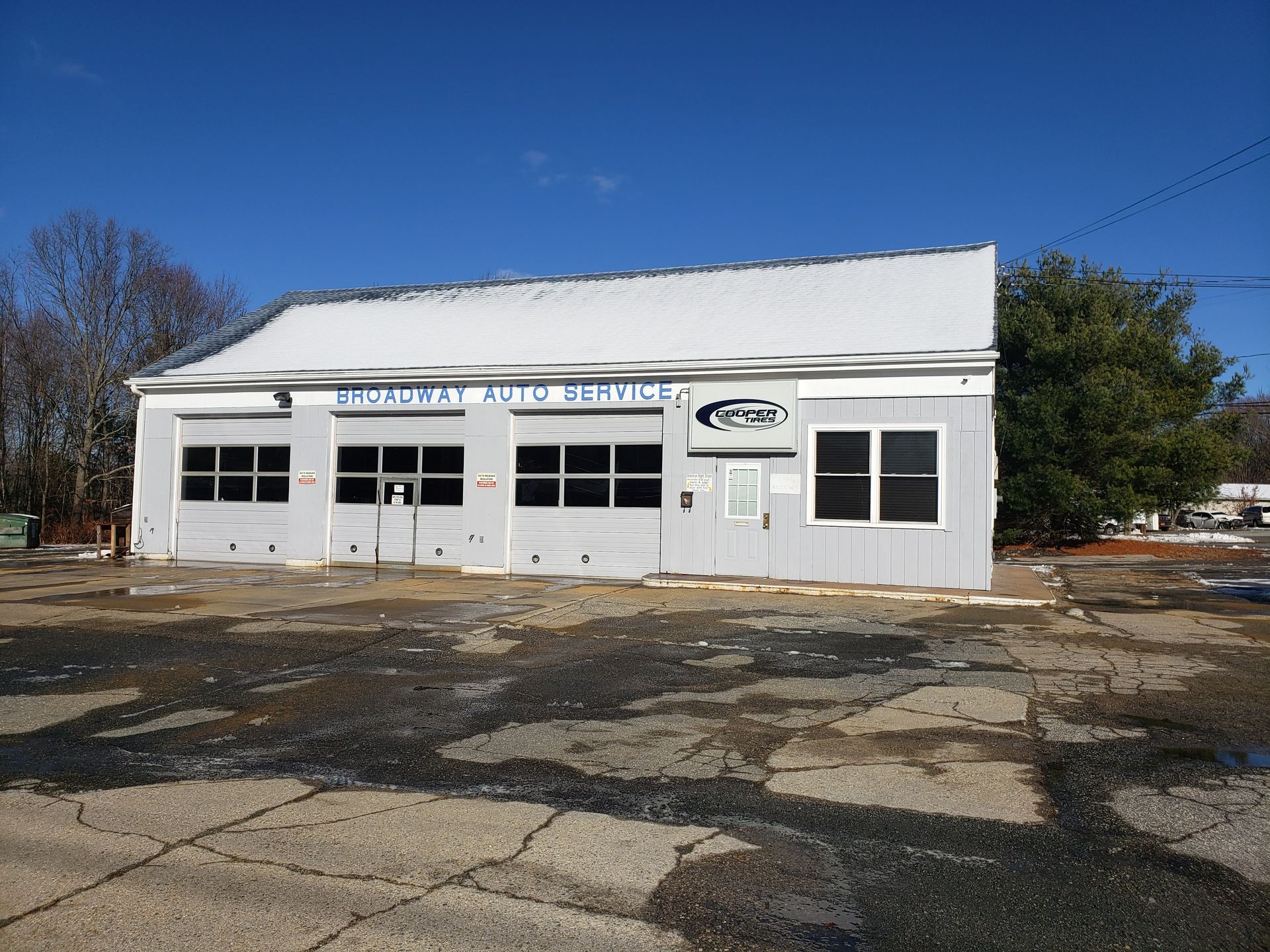 Gray auto repair shop with four garage doors, sign 