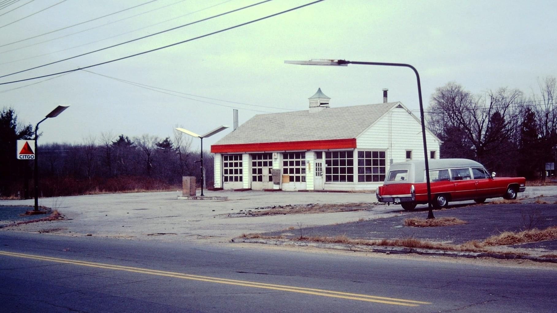 Red hearse parked outside a white gas station with a red awning. Grey sky. | Broadway Auto Service