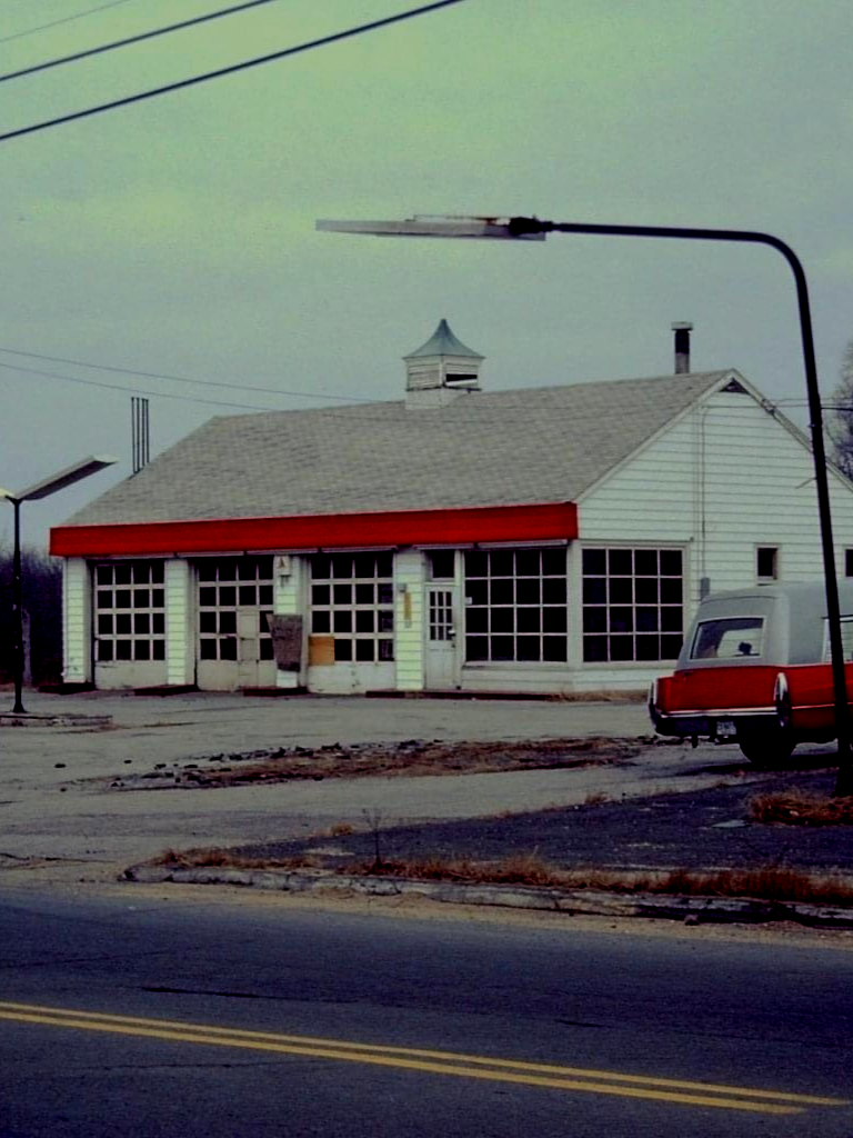White and red abandoned gas station with multiple garage doors. Red car parked outside. | Broadway Auto Service