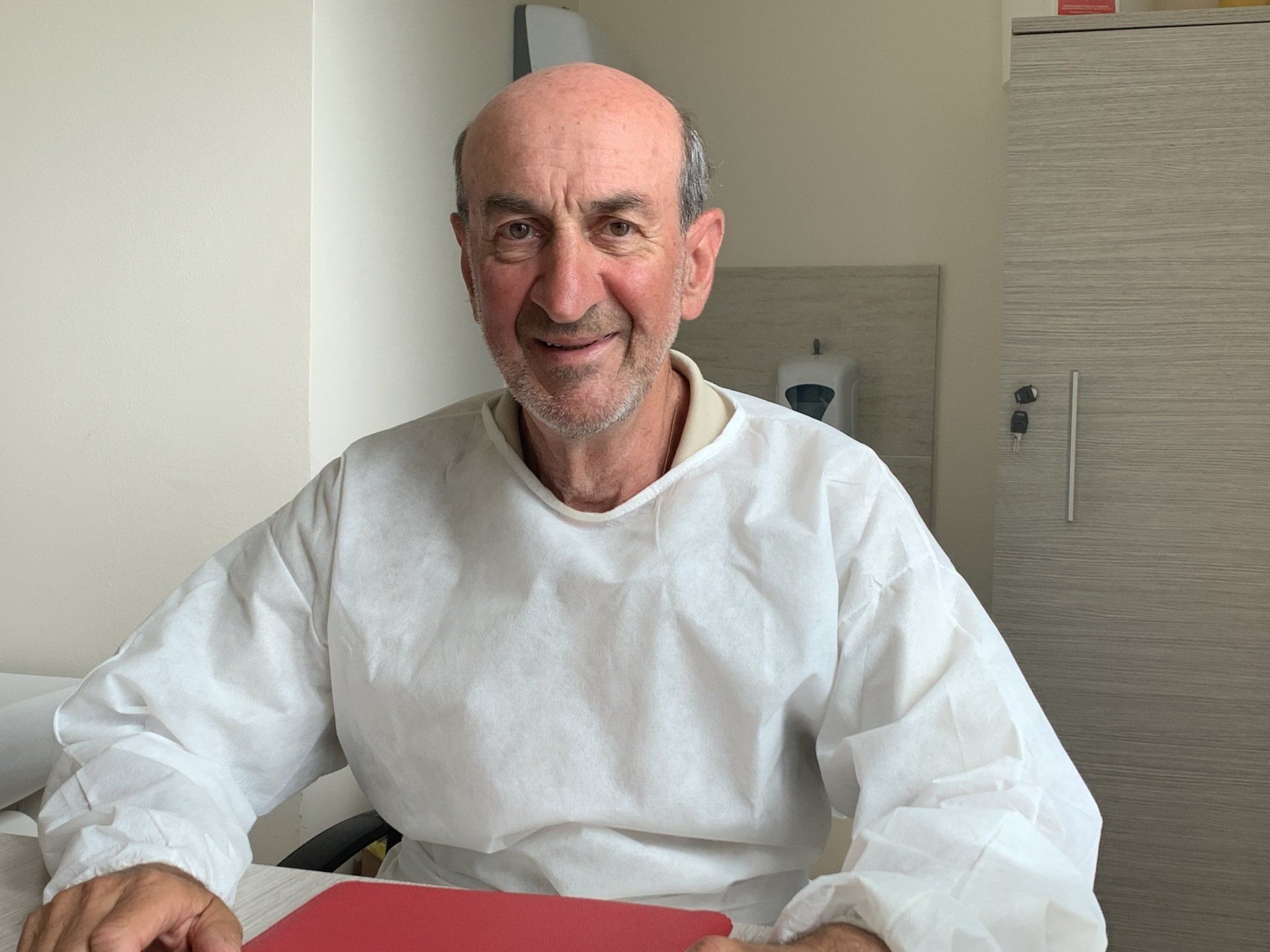 medico con camice seduto a una scrivania con in mano una cartella rossa.