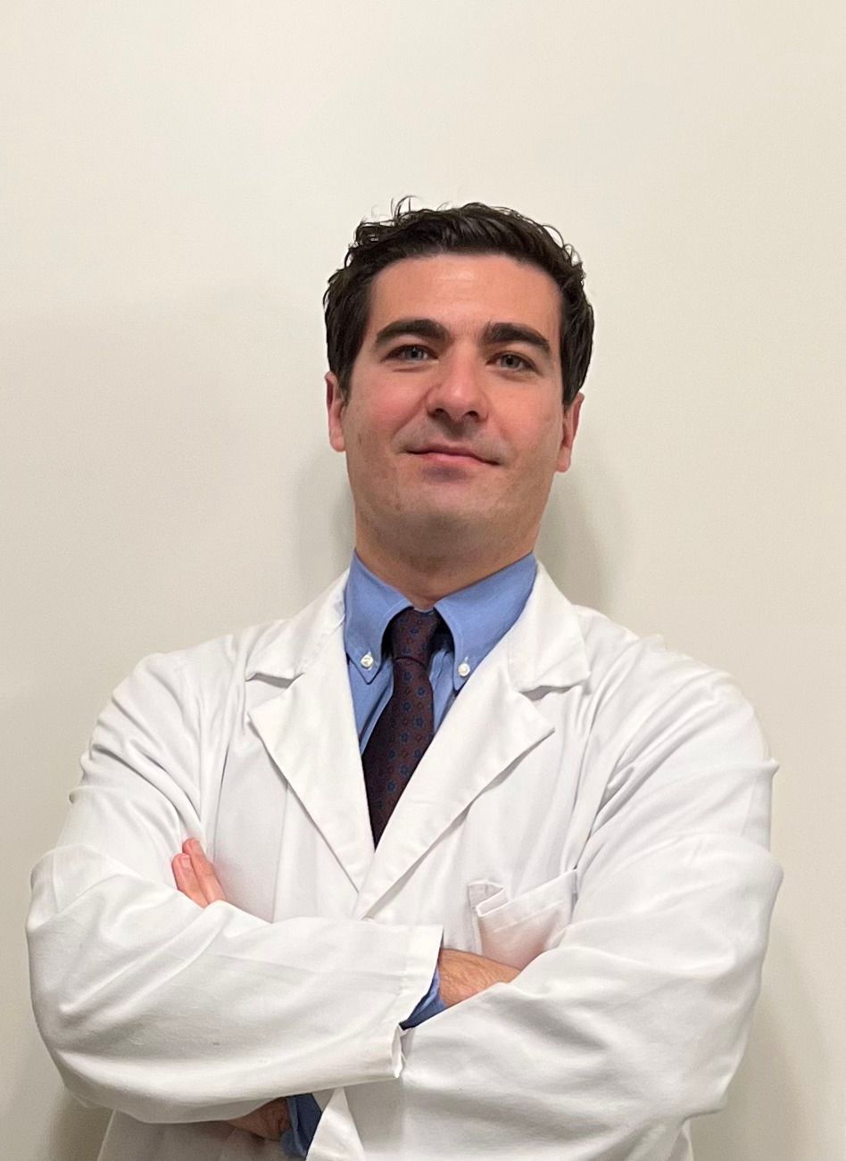 un uomo in camice da laboratorio e cravatta è in piedi con le braccia incrociate.