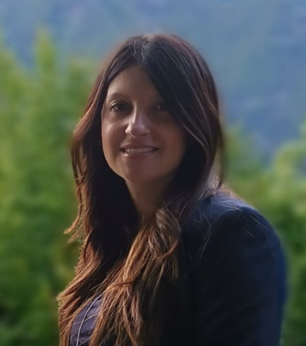 una donna con i capelli lunghi sorride alla macchina fotografica davanti a una montagna.