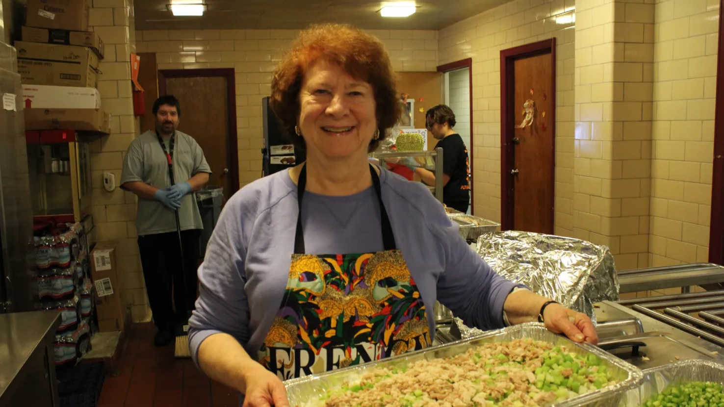 Smiling woman holds up tray of salad