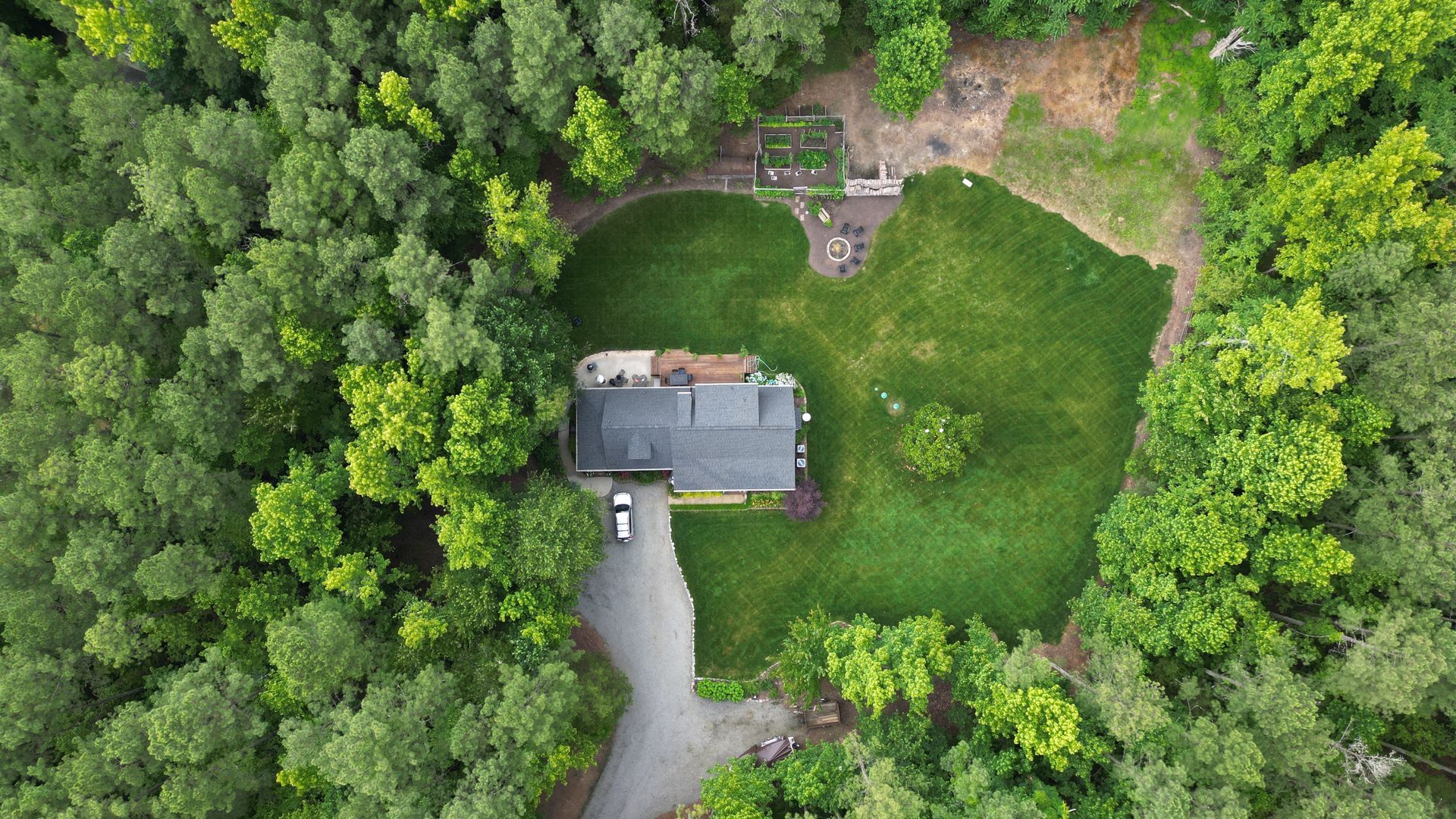 An aerial view of a house in the middle of a forest surrounded by trees.
