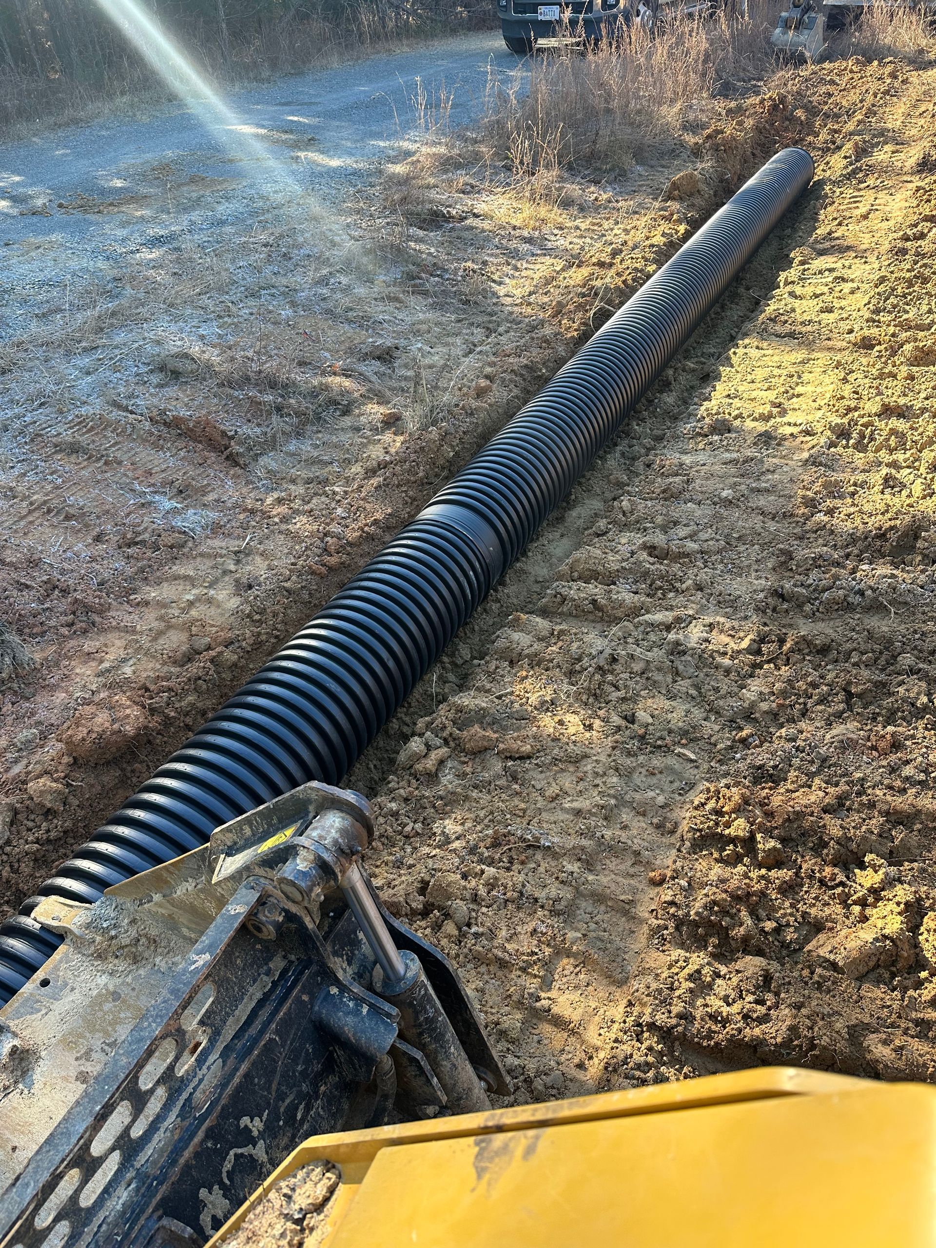 A large black pipe is laying in the dirt next to a yellow truck.